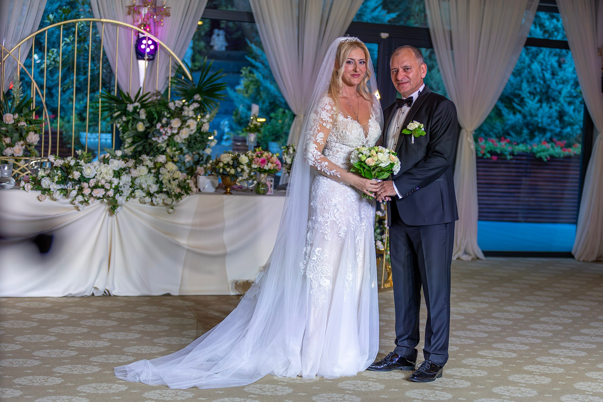 Marius și Daniela pe ringul de dans pozează în fața mesei festive la nuntă, decor floral