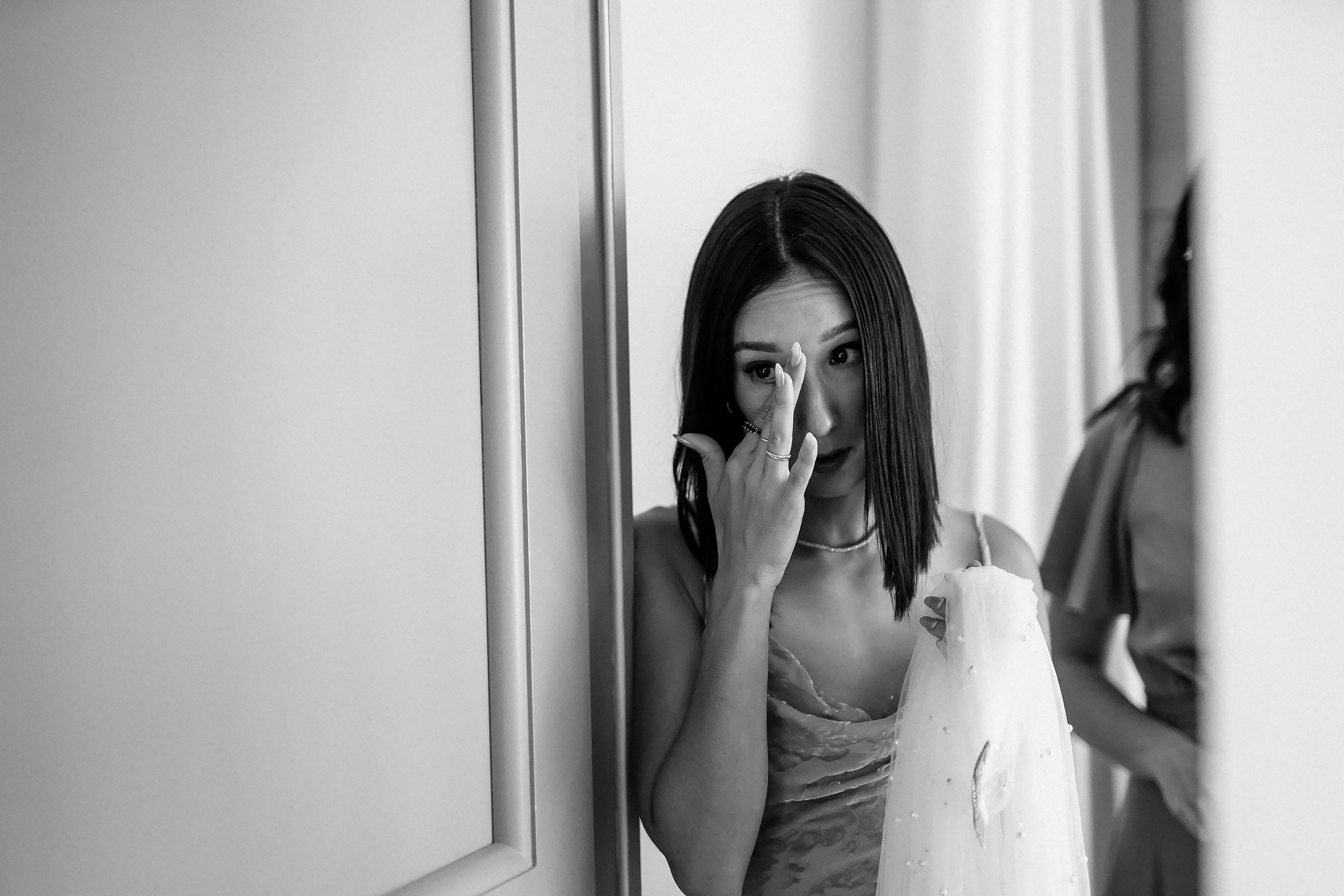 An emotional bridesmaid wipes tears while holding part of a wedding dress in a heartfelt moment.