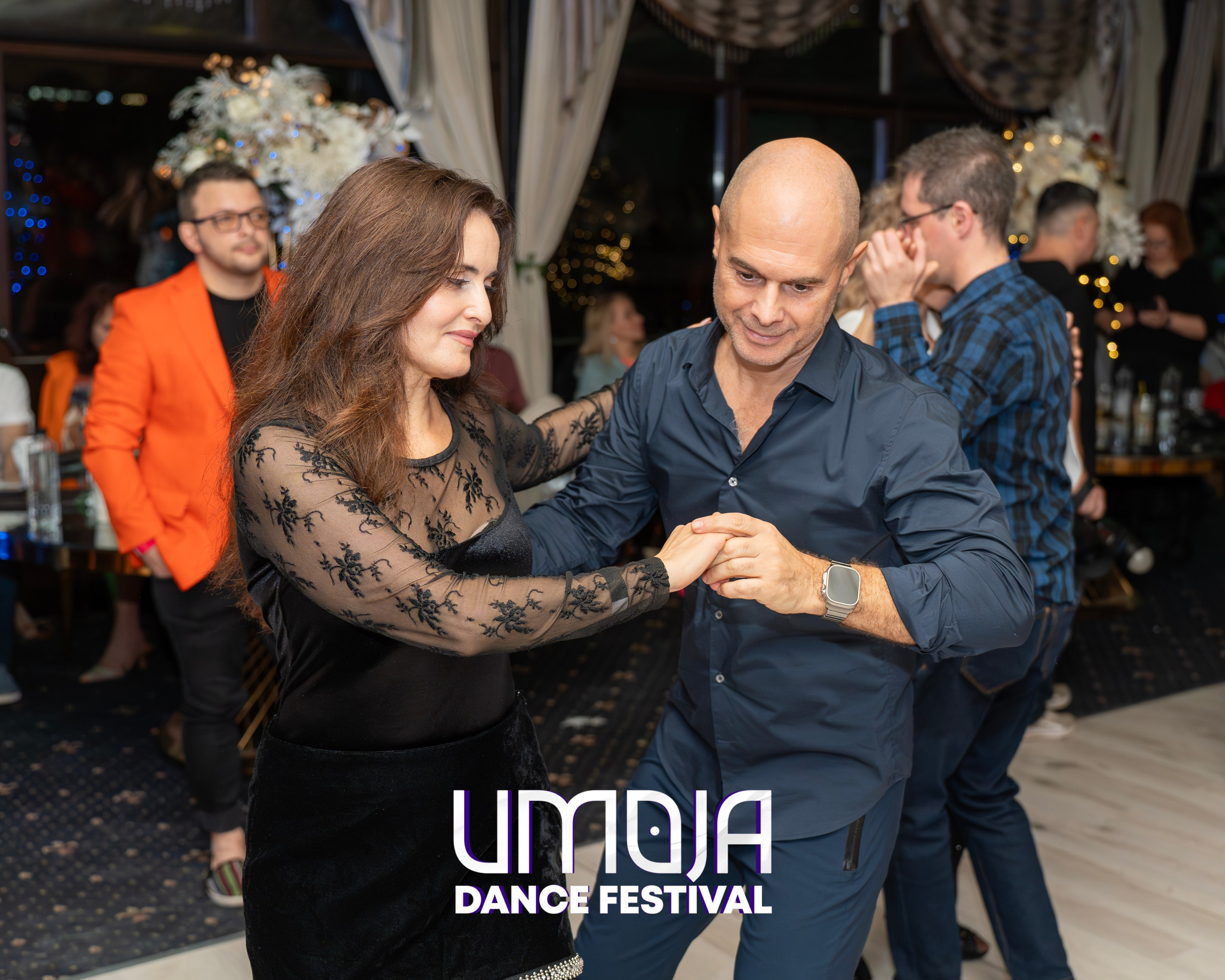 Man and woman dancing together at an indoor dance event with other people in the background.