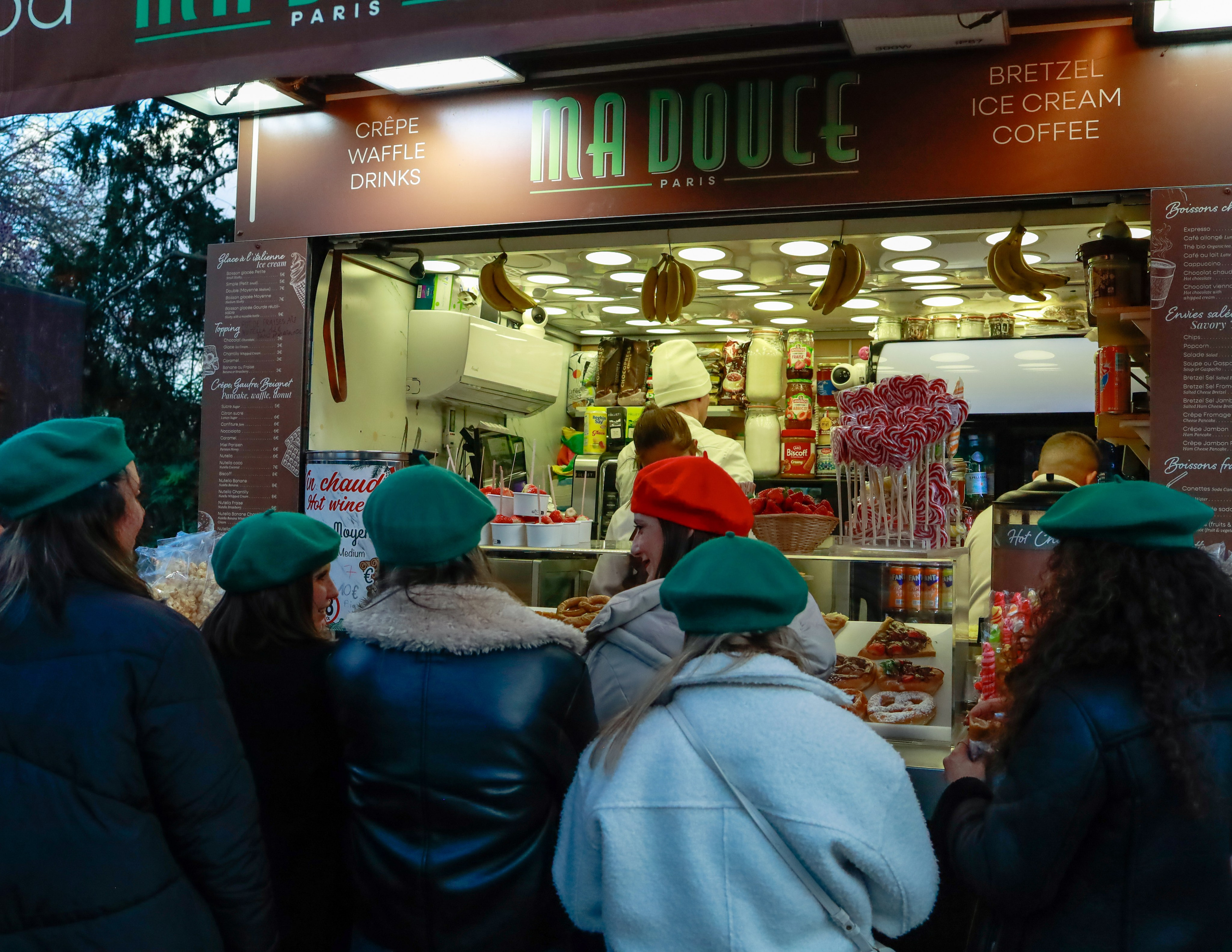 a crepe stand with a group of tourists women wearing green beret except one wearing a red one