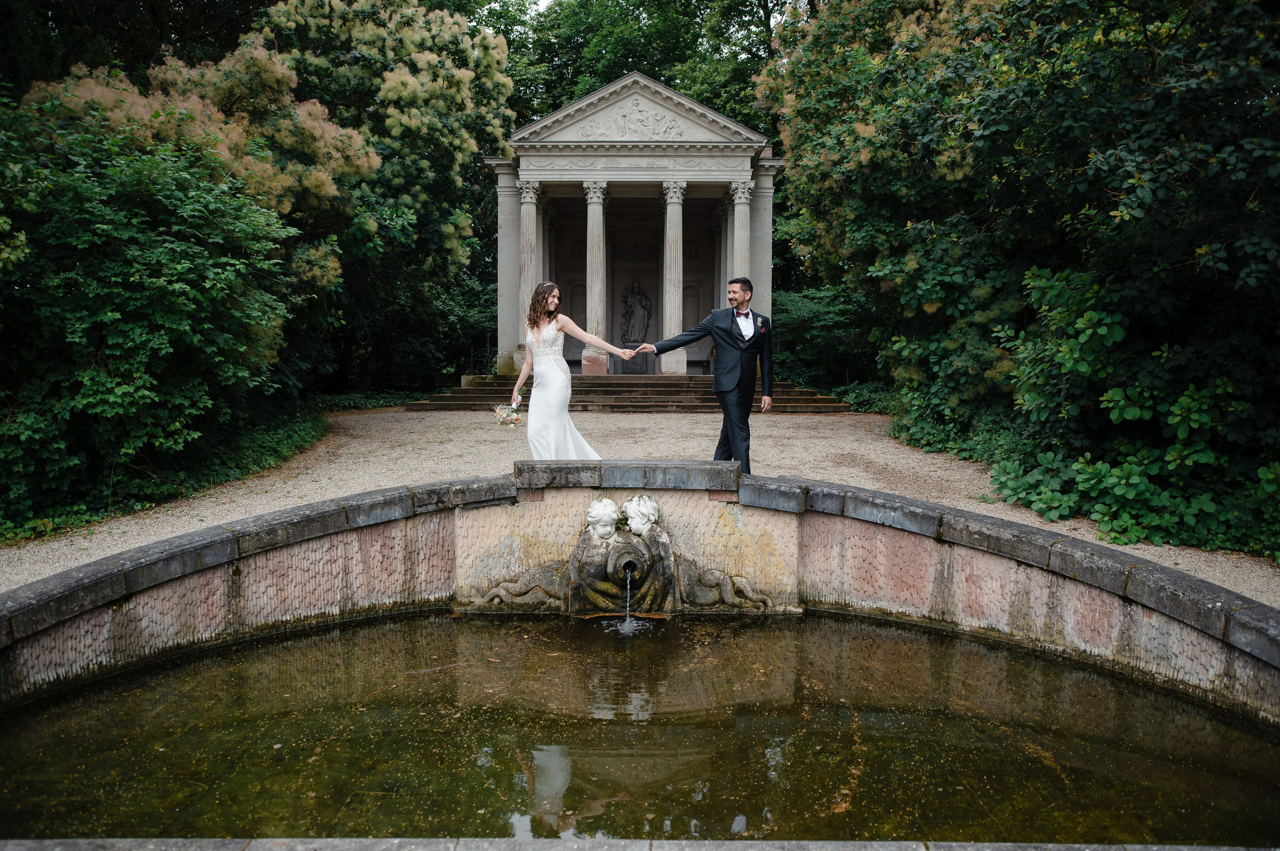 Brautpaar beim Spaziergang vor klassischer Architektur im Schlossgarten