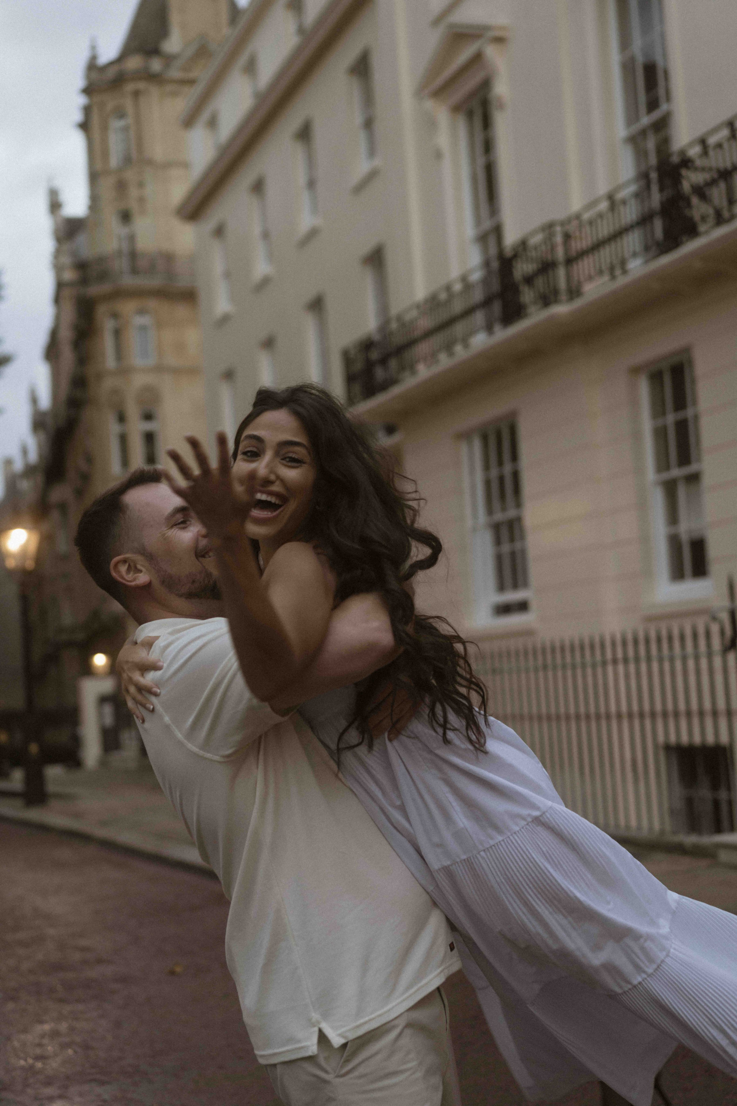 Couple laughing and spinning in London street, candid engagement photography