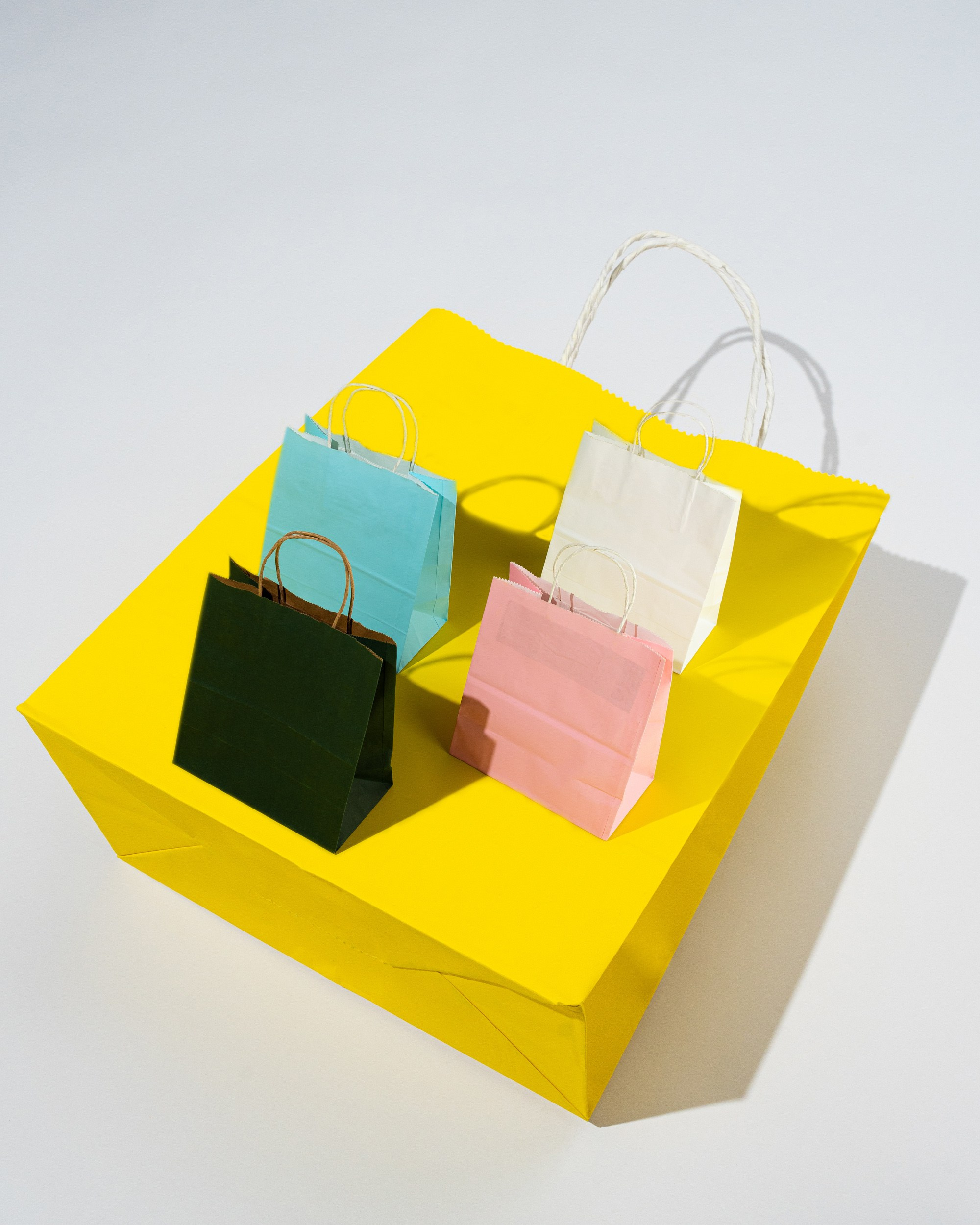 Sarı fon üzərində müxtəlif rəngli kağız hədiyyə torbaları – mavi, ağ, çəhrayı və yaşıl.