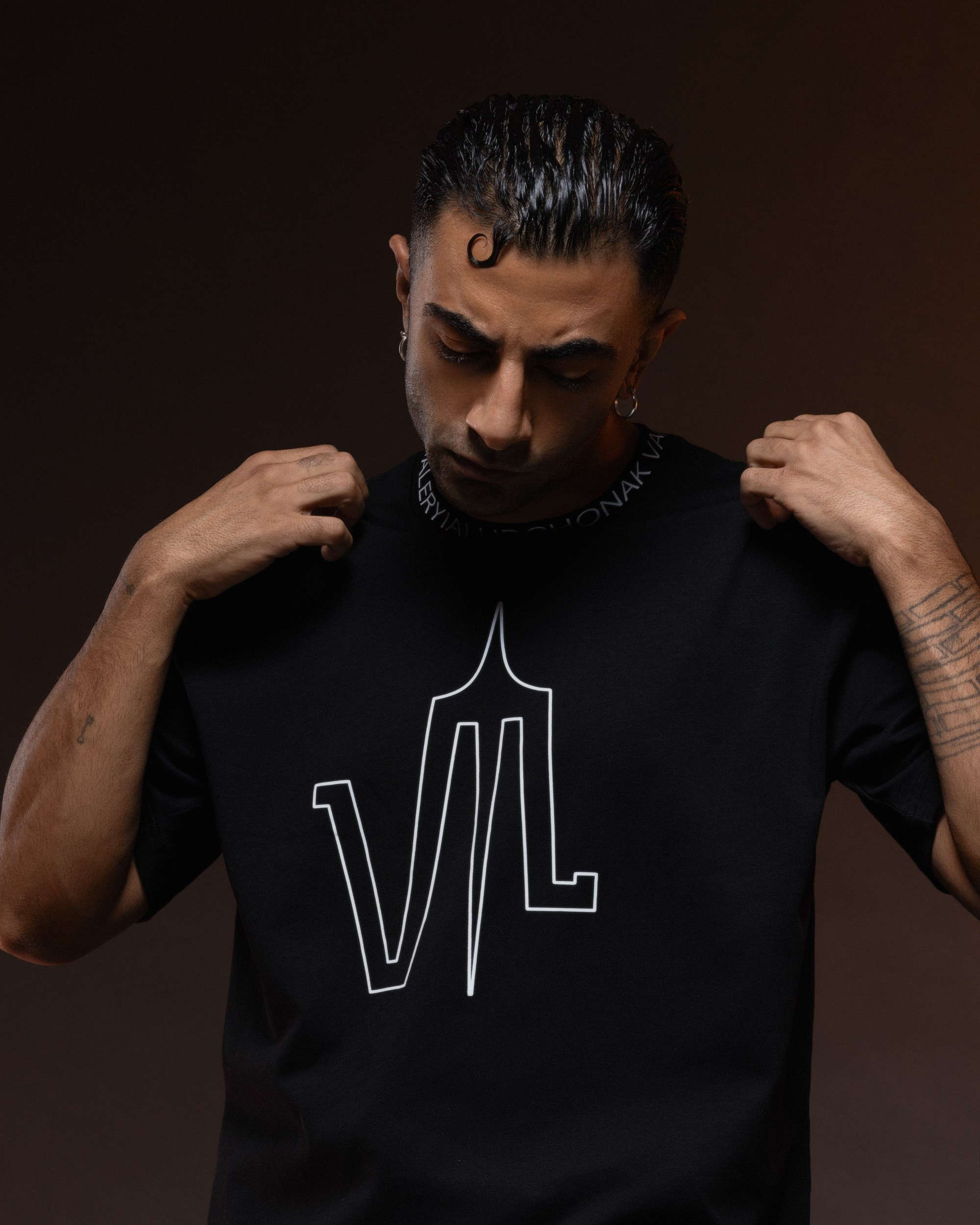 Fashion model wearing a black t-shirt with a unique graphic, posing in a dimly lit studio