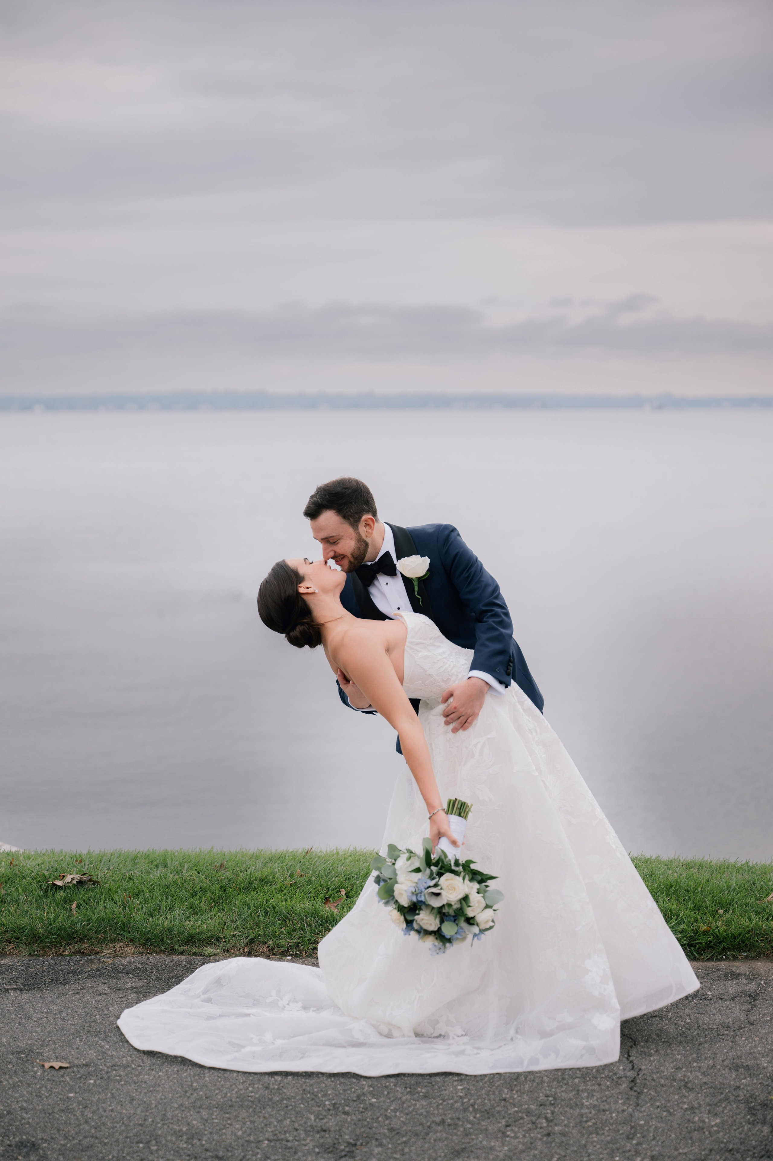 a bride and groom kissing on the shore of a lake