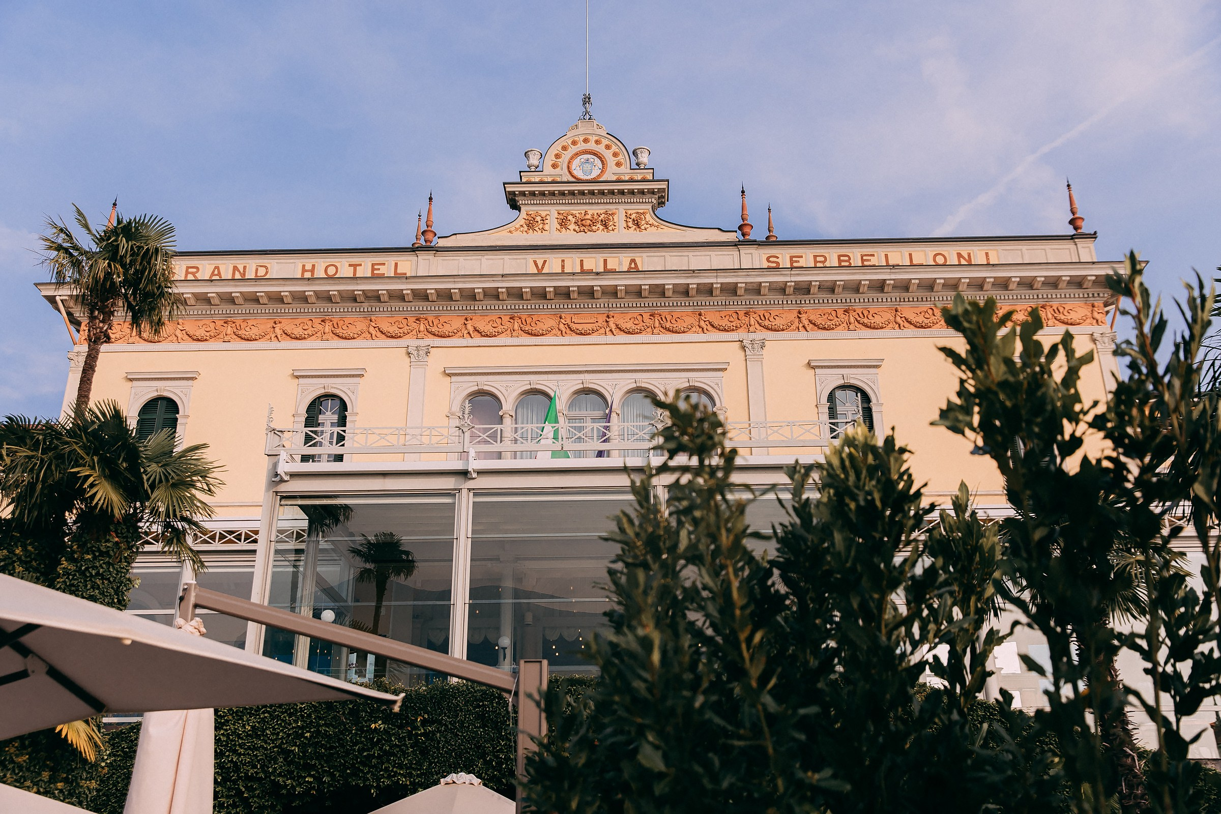 Another stunning view of the “Grand Hotel Villa Serbelloni,” framed by lush greenery and umbrellas, exuding timeless charm.