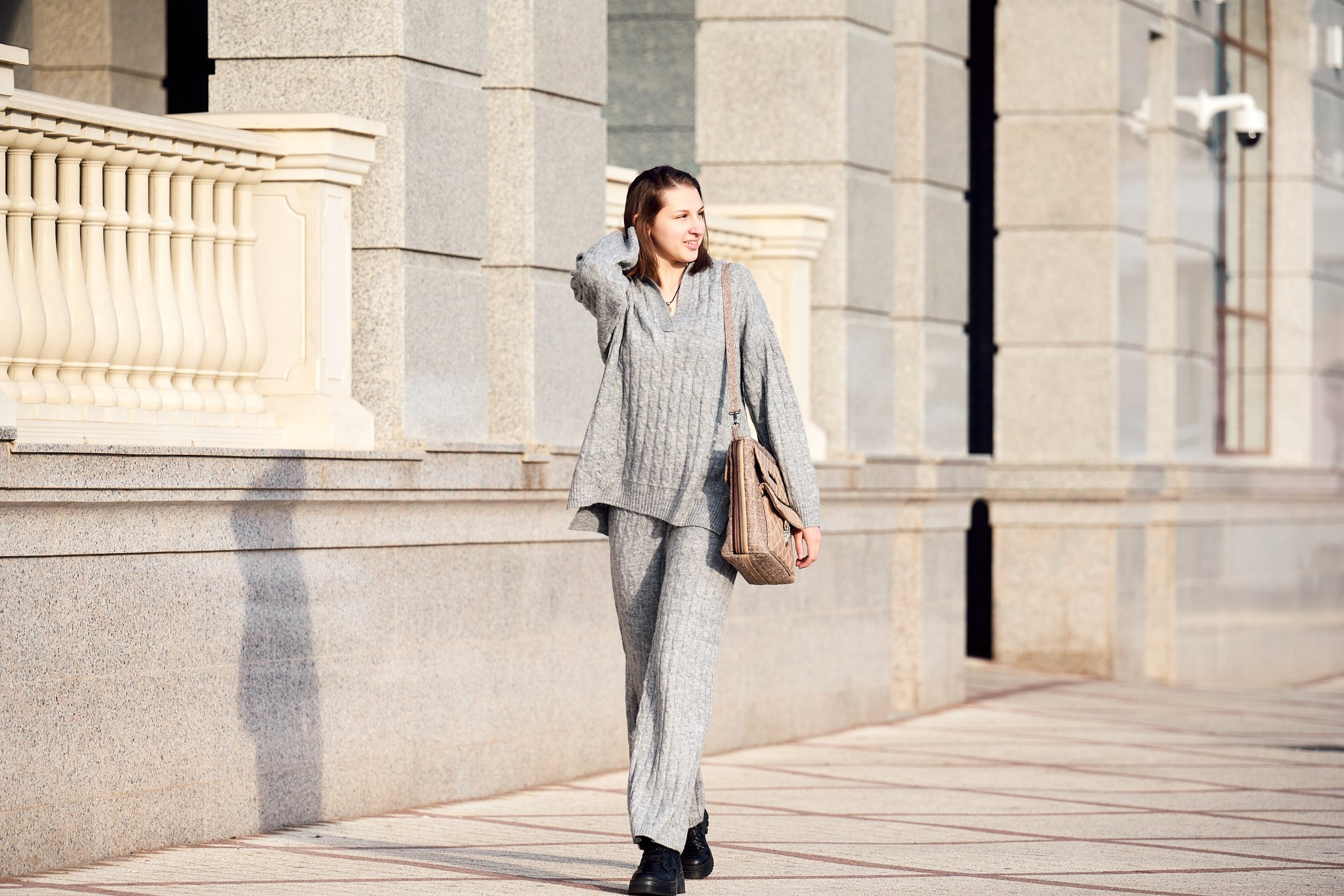 Портрет девушки в сером вязанном костюме и бежевой сумкой с распущенными каштановыми волосами