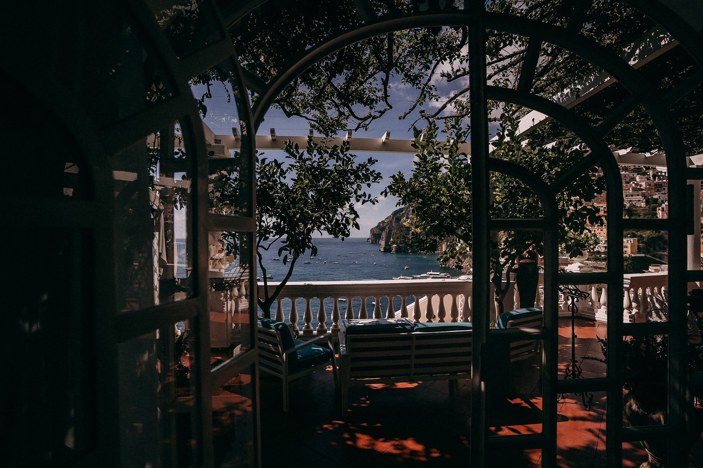 A stunning ocean view framed by the open doors of Villa Bohème, with a balcony overlooking the sea and distant cliffs of Positano.