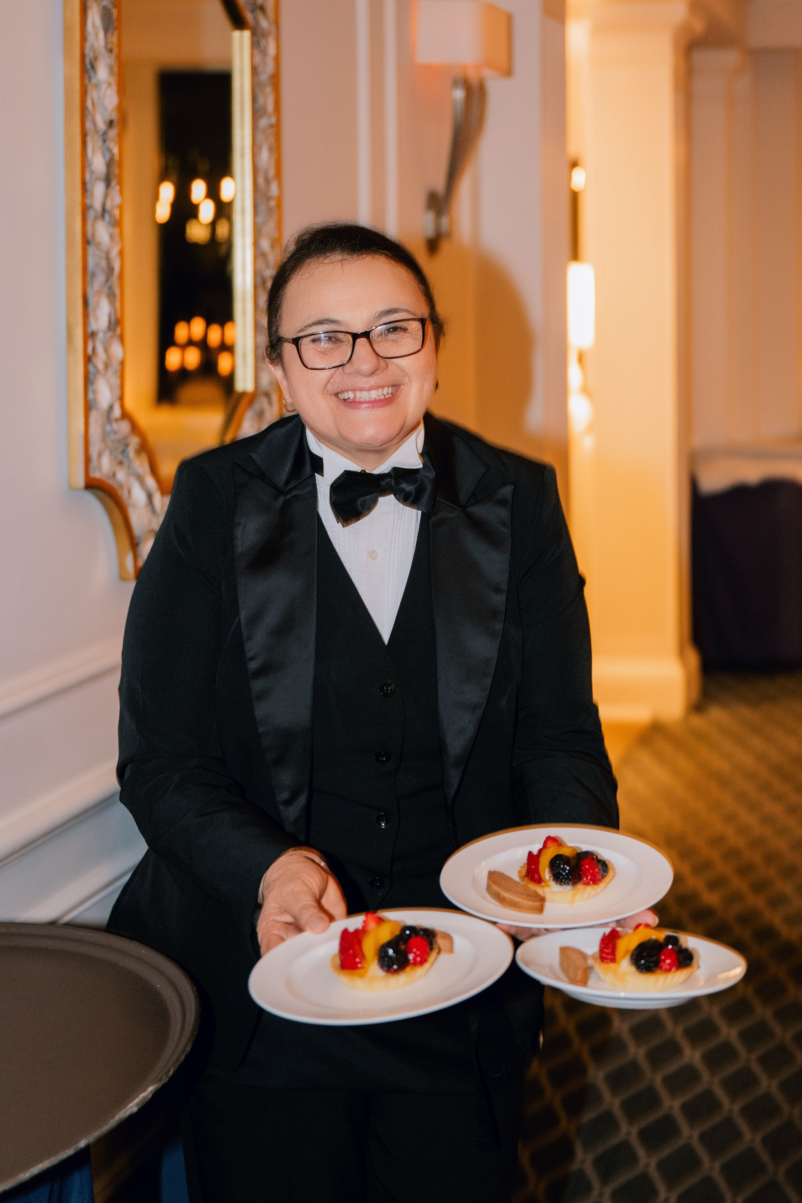 a woman in a tuxed suit holding two plates of food