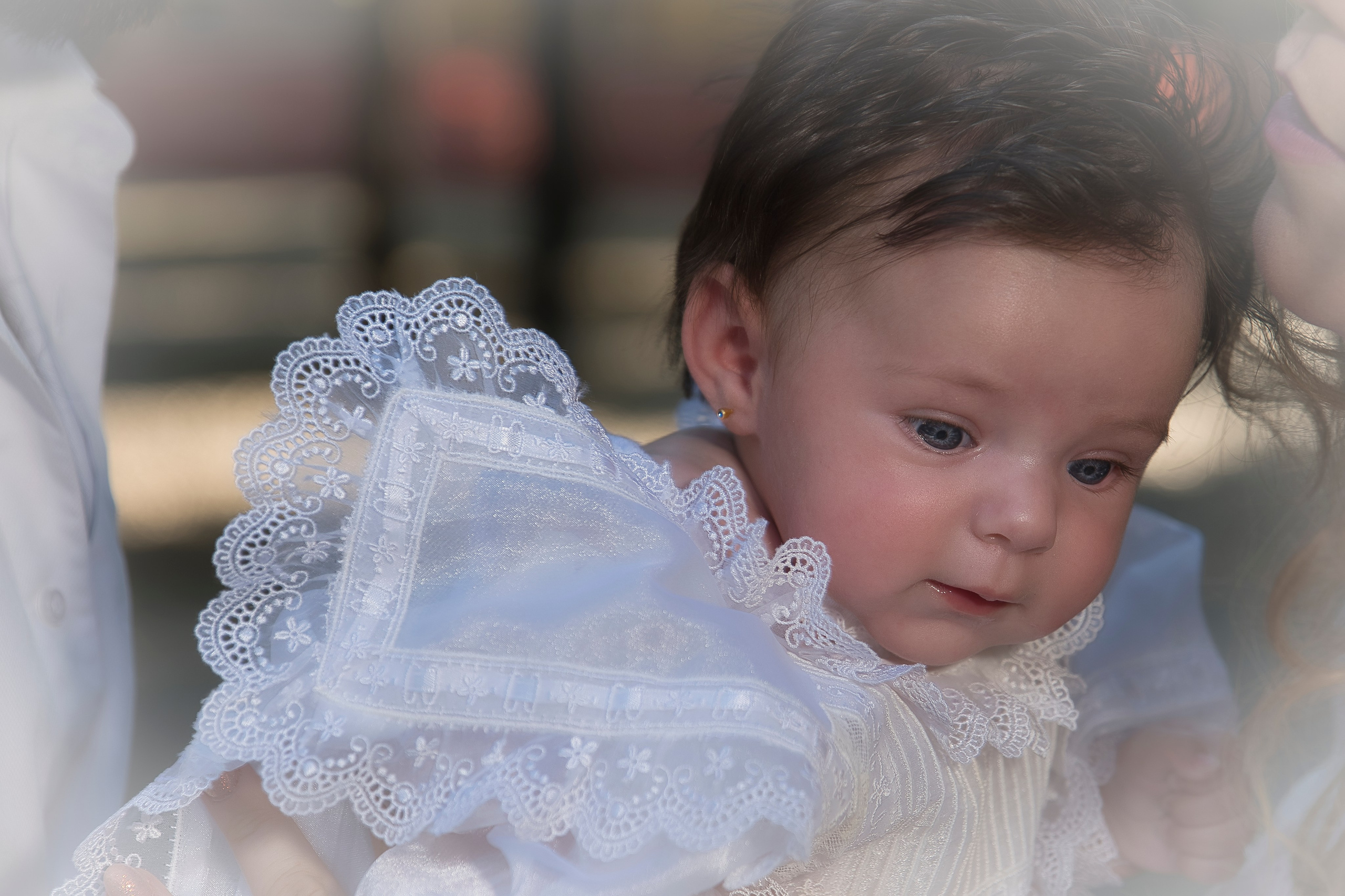 Niña vestida con traje de bautizo blanco, sostenida por sus padres en la iglesia.