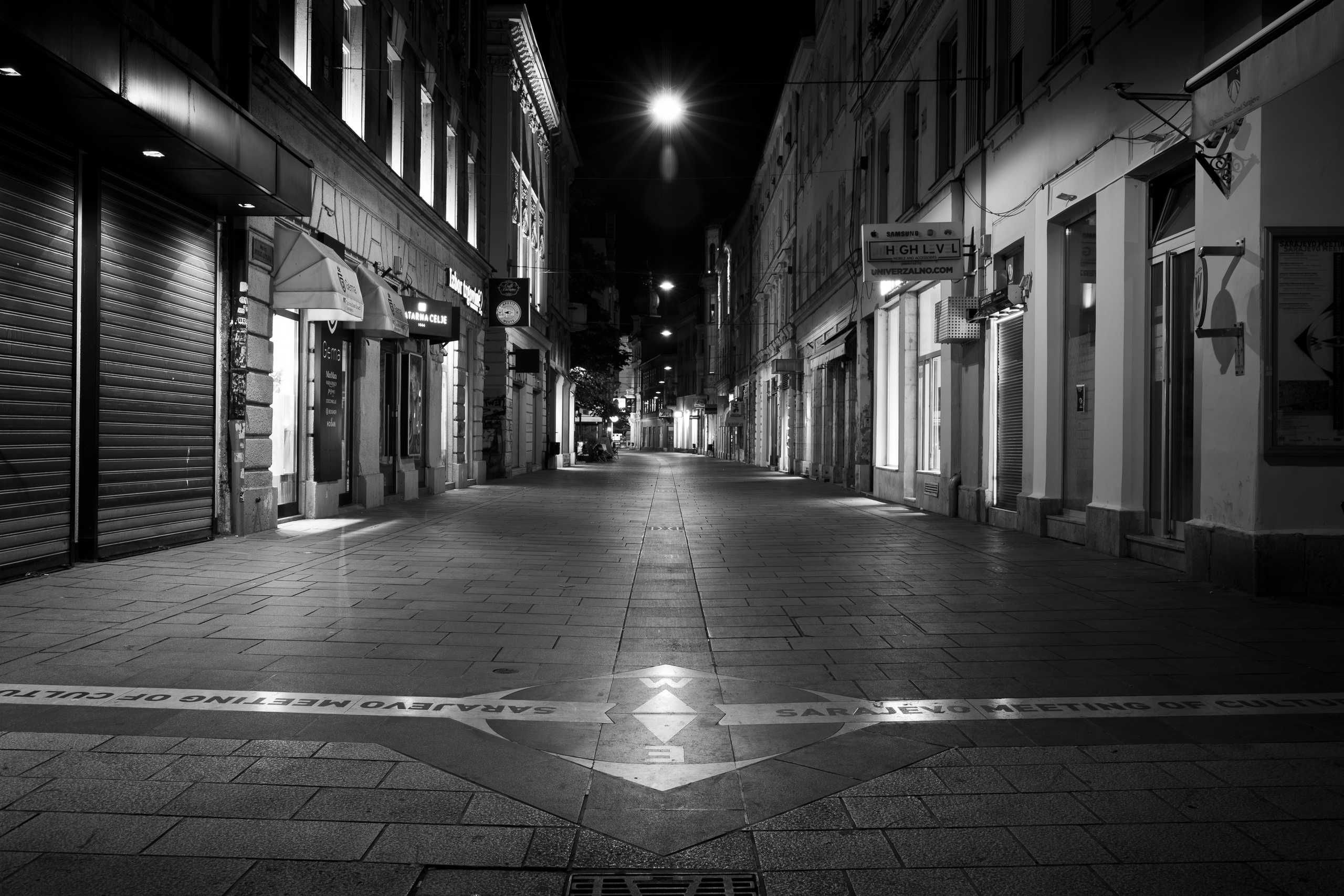 Crno-bijela noćna fotografija Sarajeva – ulice, svjetla i refleksije grada u tišini.