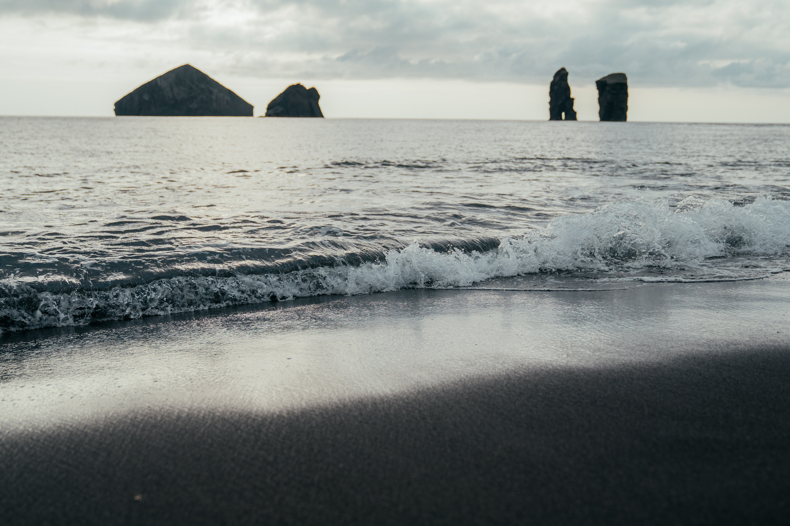 Černá pláž a skály v oceánu na ostrově Sao Miguel za večerního světla.