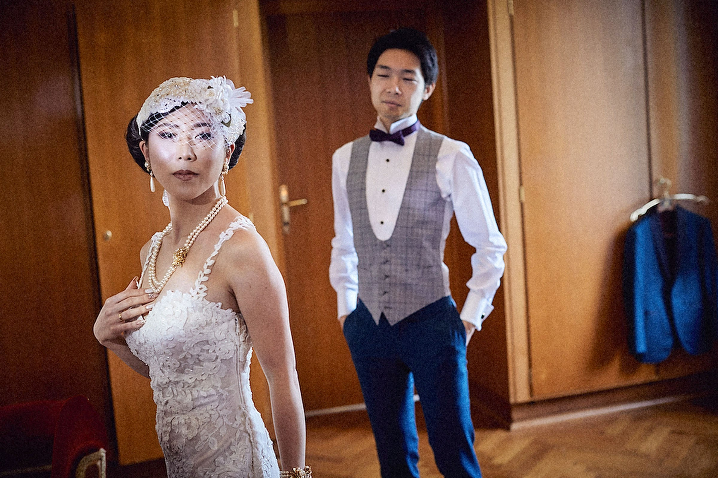 A stylish Japanese bride looks into the mirror as she lovingly touches her fine jewelry as her groom stands watching behind her.