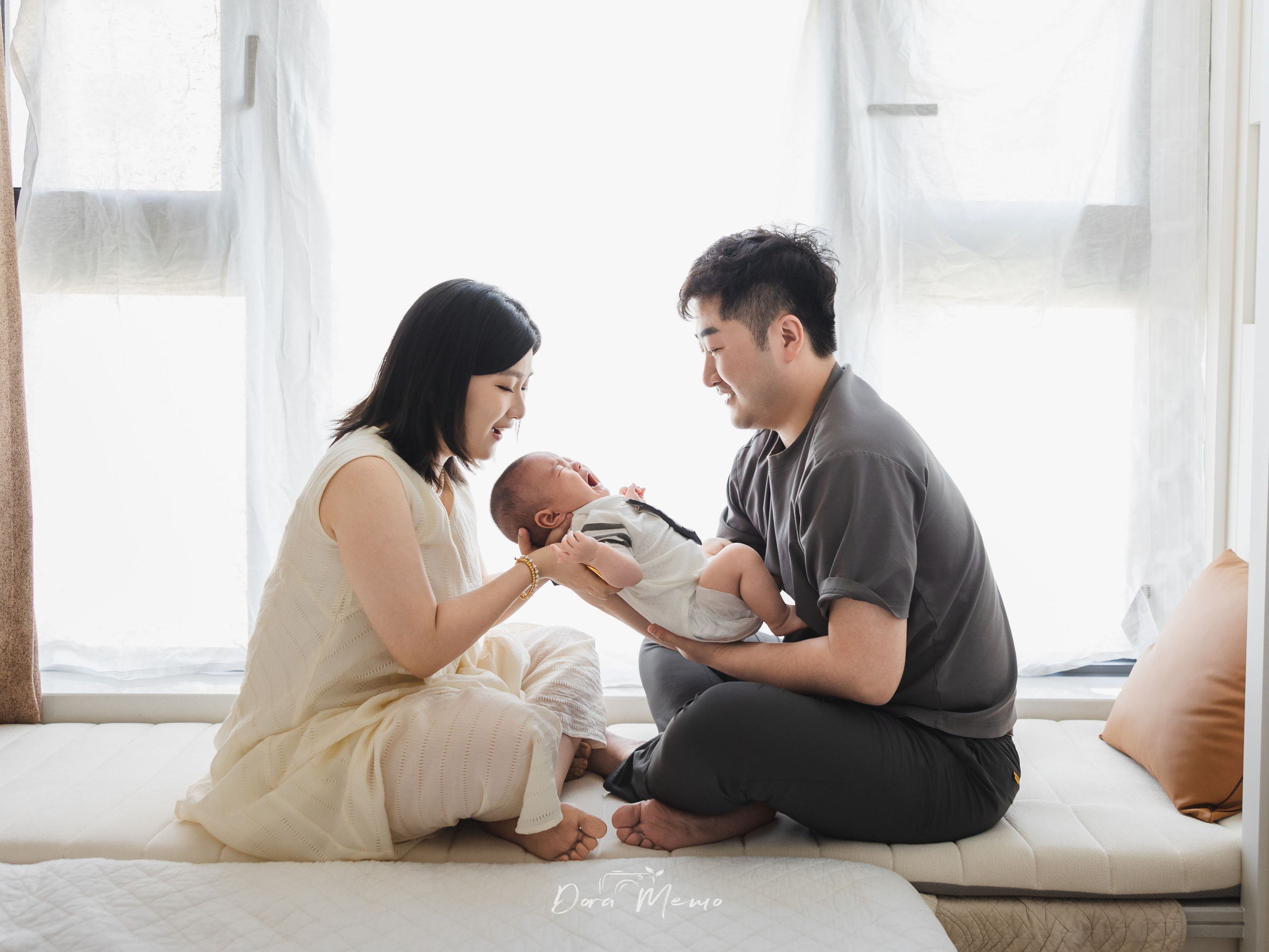 A father kissing his baby while the mother smiles nearby in a warm family photography moment.