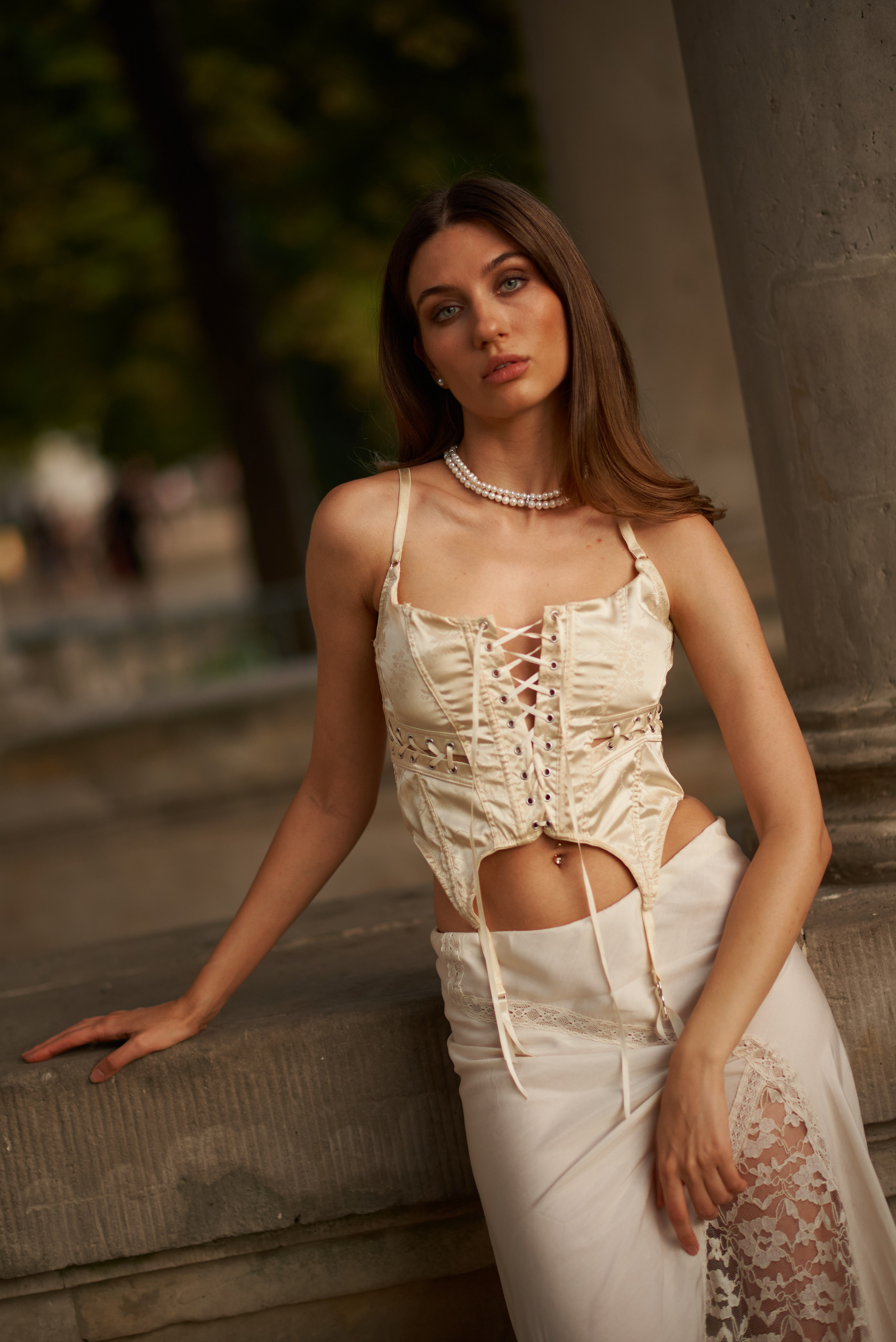 Погляд крізь час – Дівчина в розкішному корсеті й спідниці з мереживом спирається на кам'яну колону в парку Лазенкі. Її погляд мрійливо спрямований у далечінь.