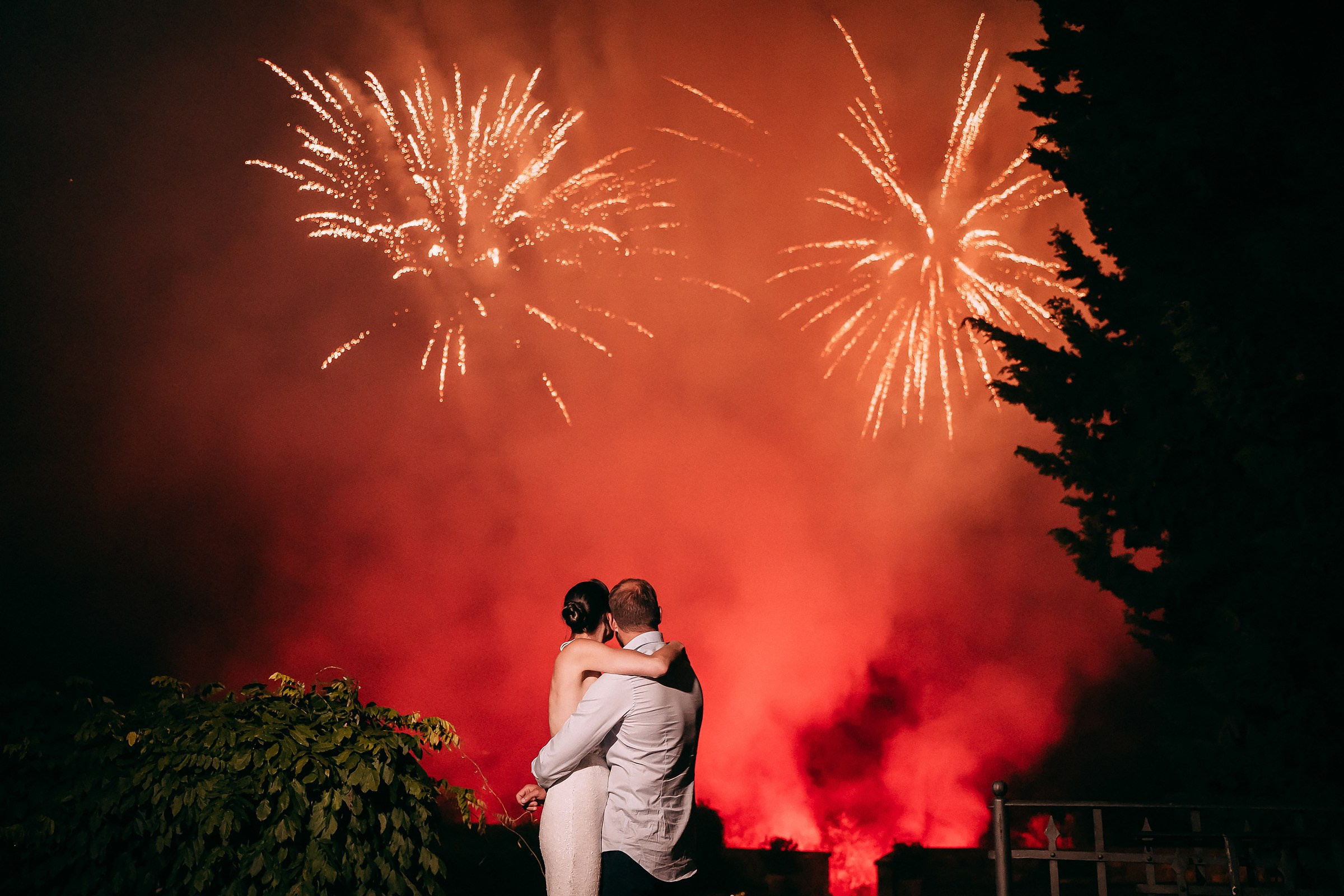 The couple gazes lovingly at the sky as brilliant gold fireworks light up the dark, creating a magical, celebratory moment.