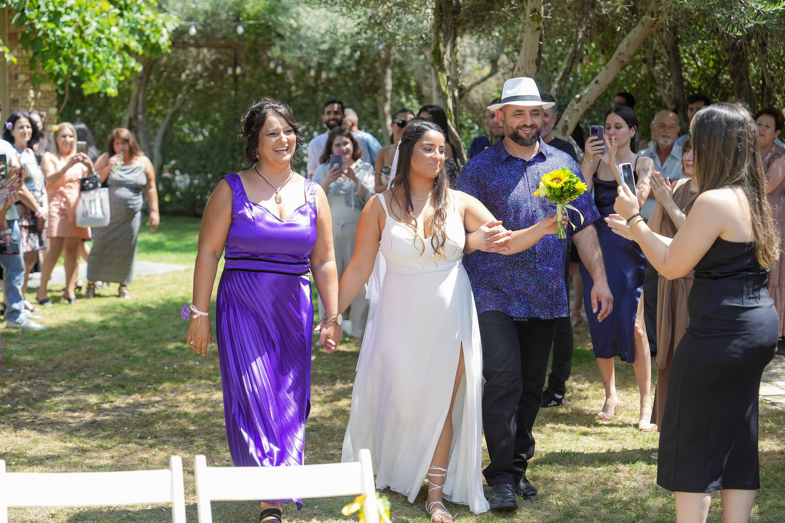 Bride walks to the chuppah with her parents at Villa Nona Caesarea and gives a sunflower to her friend.