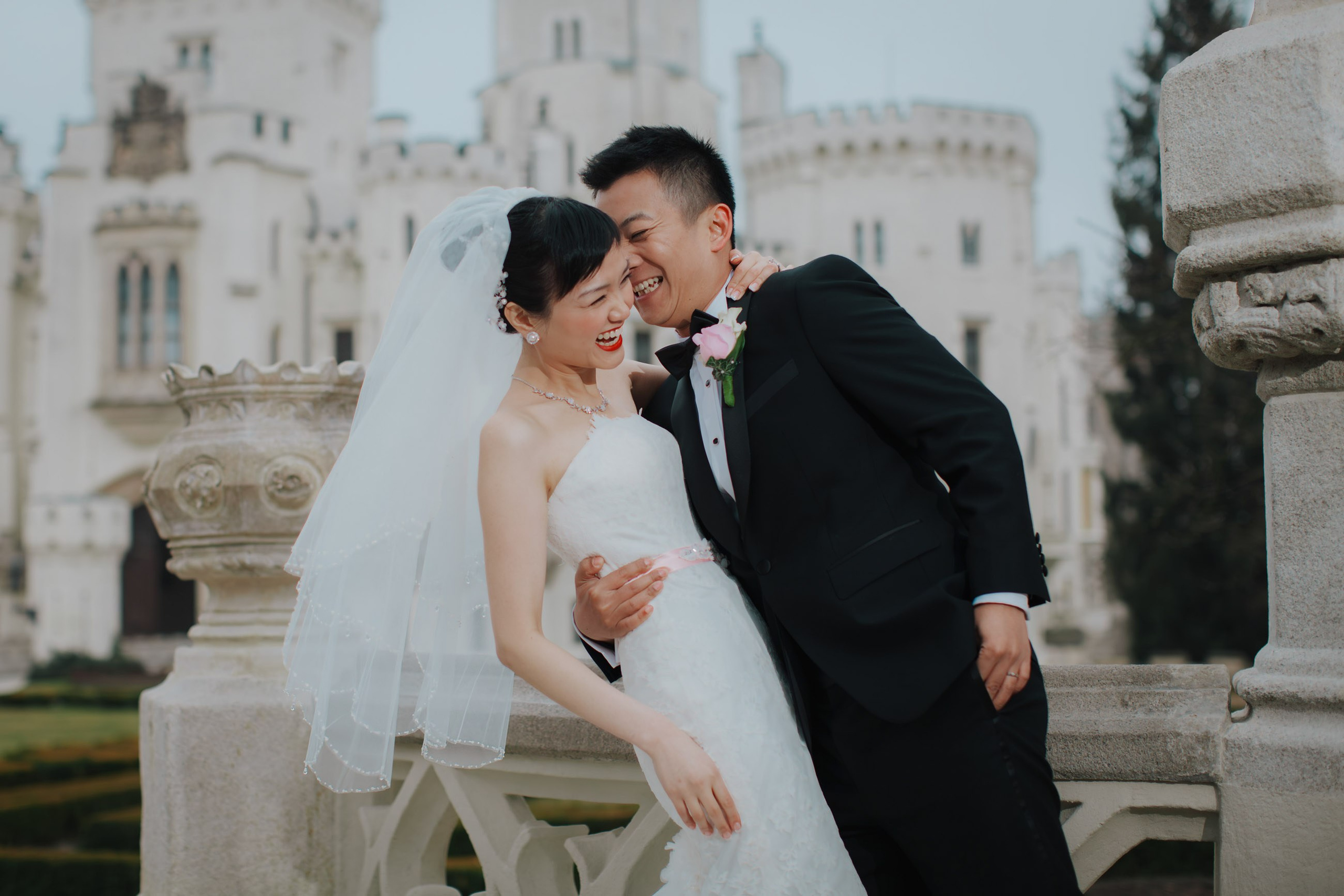 A smiling groom grabs his laughing Hong Kong bride on the grounds of the historic Castle Hluboka where they had earlier held thier intimate destination wedding in Czechia.