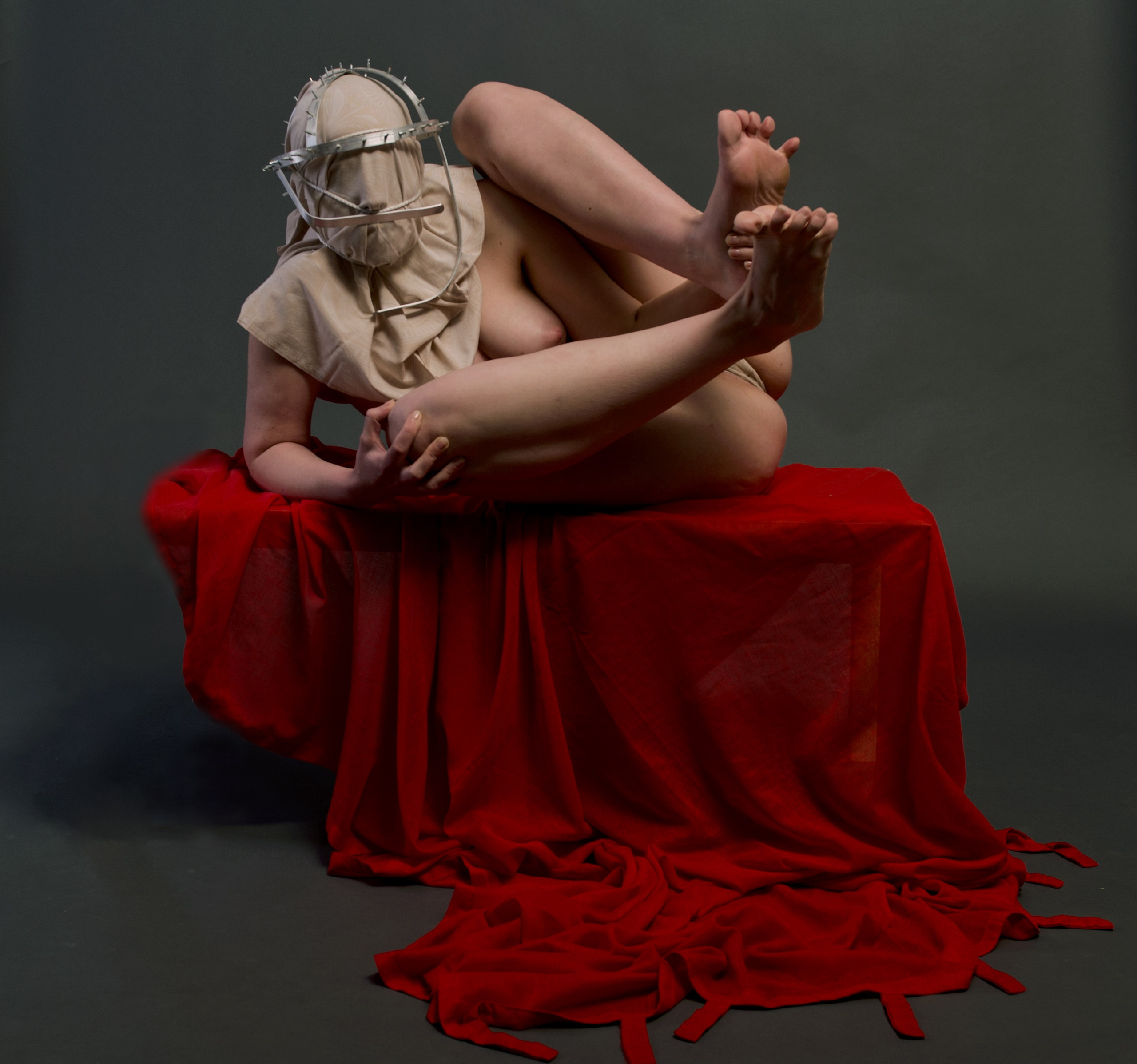 Surreal photograph of a nude female figure with a concealed face, seated on a red-draped platform adorned with a crown-like object, from Leni Smoragdova's 'Figures Collection: Prophet Version' (2020).