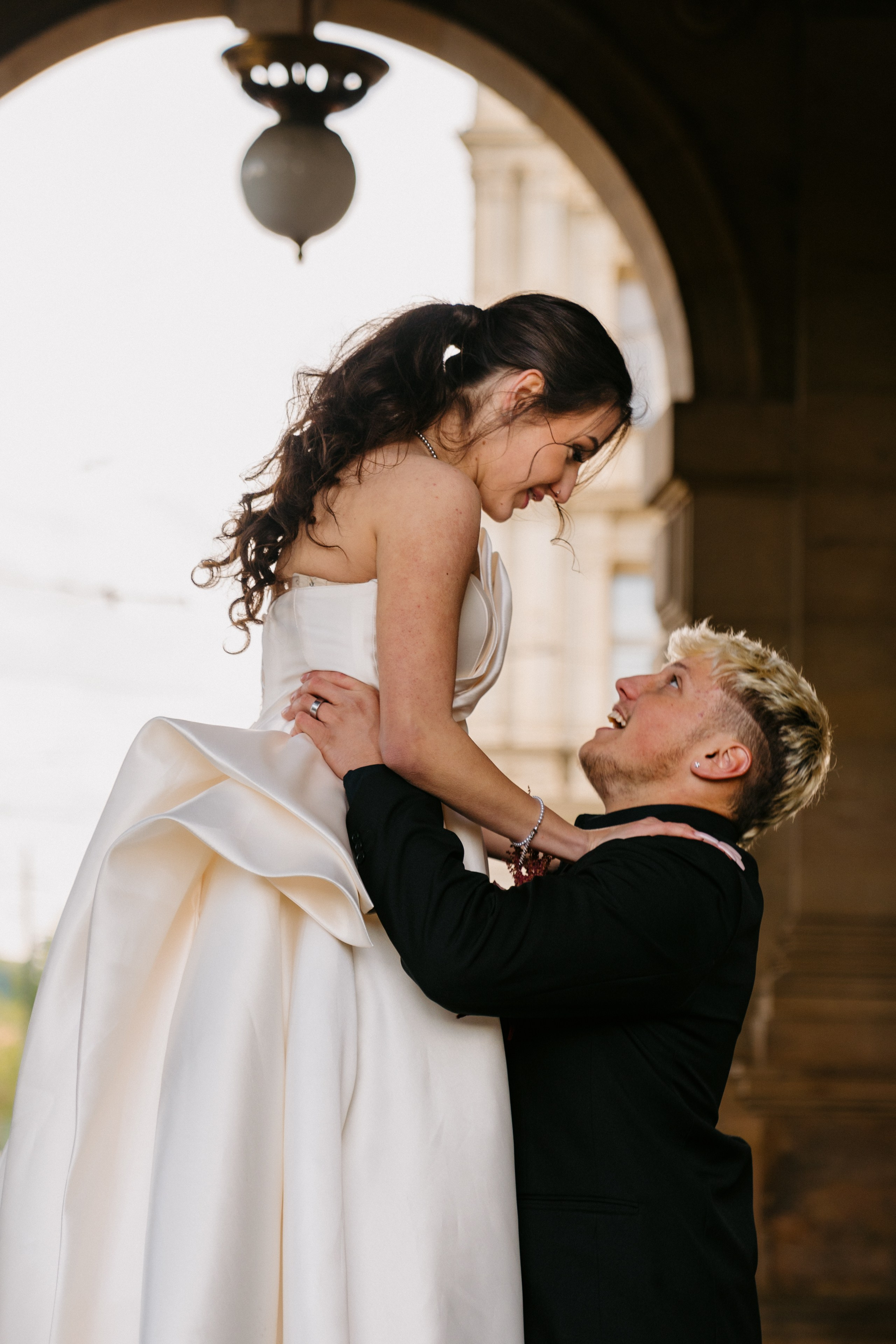 Intimní svatební focení v Praze, spontánní moment, kdy ženich zvedá nevěstu pod historickým podloubím Národního divadla. přirozené emoce a pohyb.