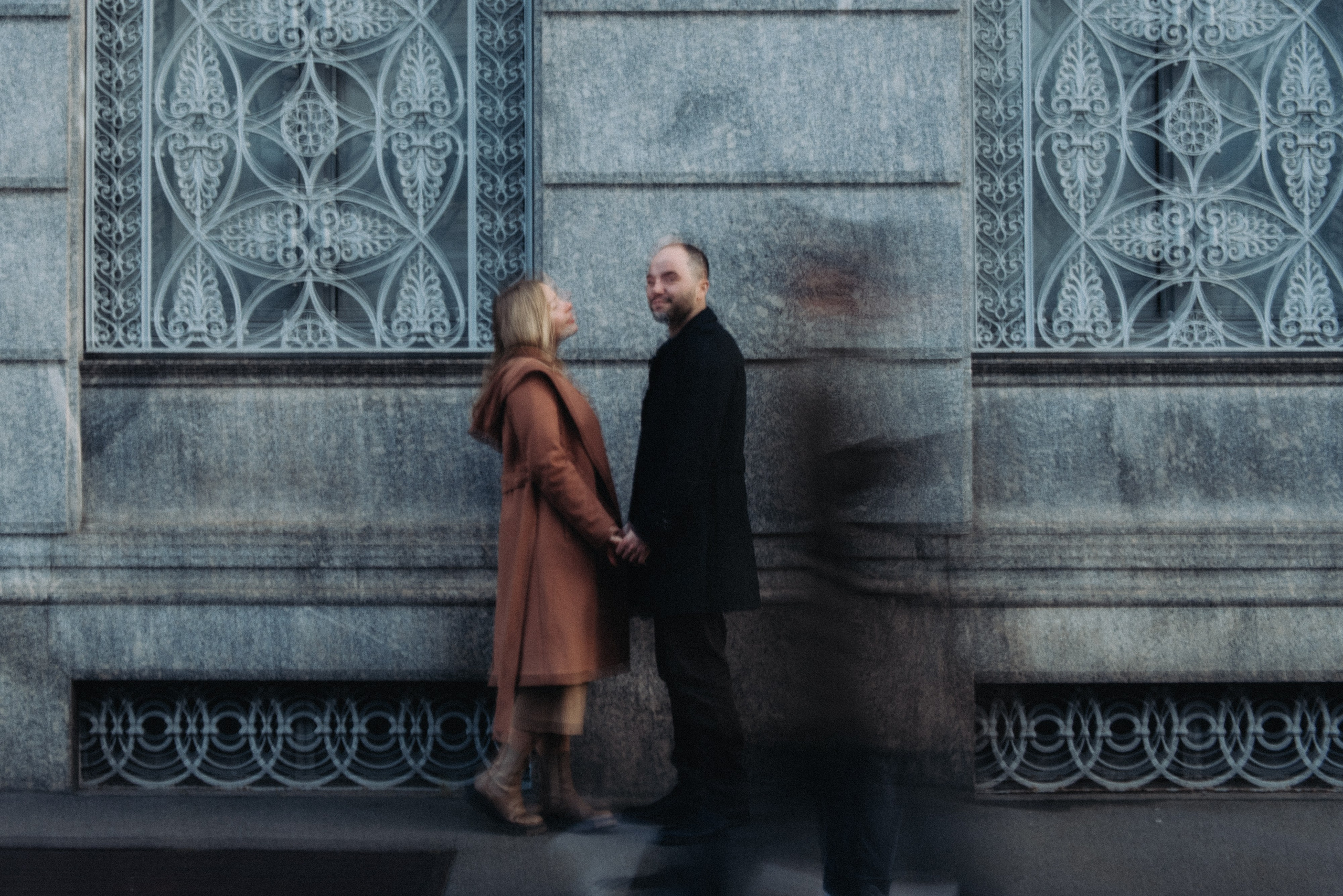Couple standing against a historic stone facade with motion blur of pedestrians in Milan. Milan couple photo session.