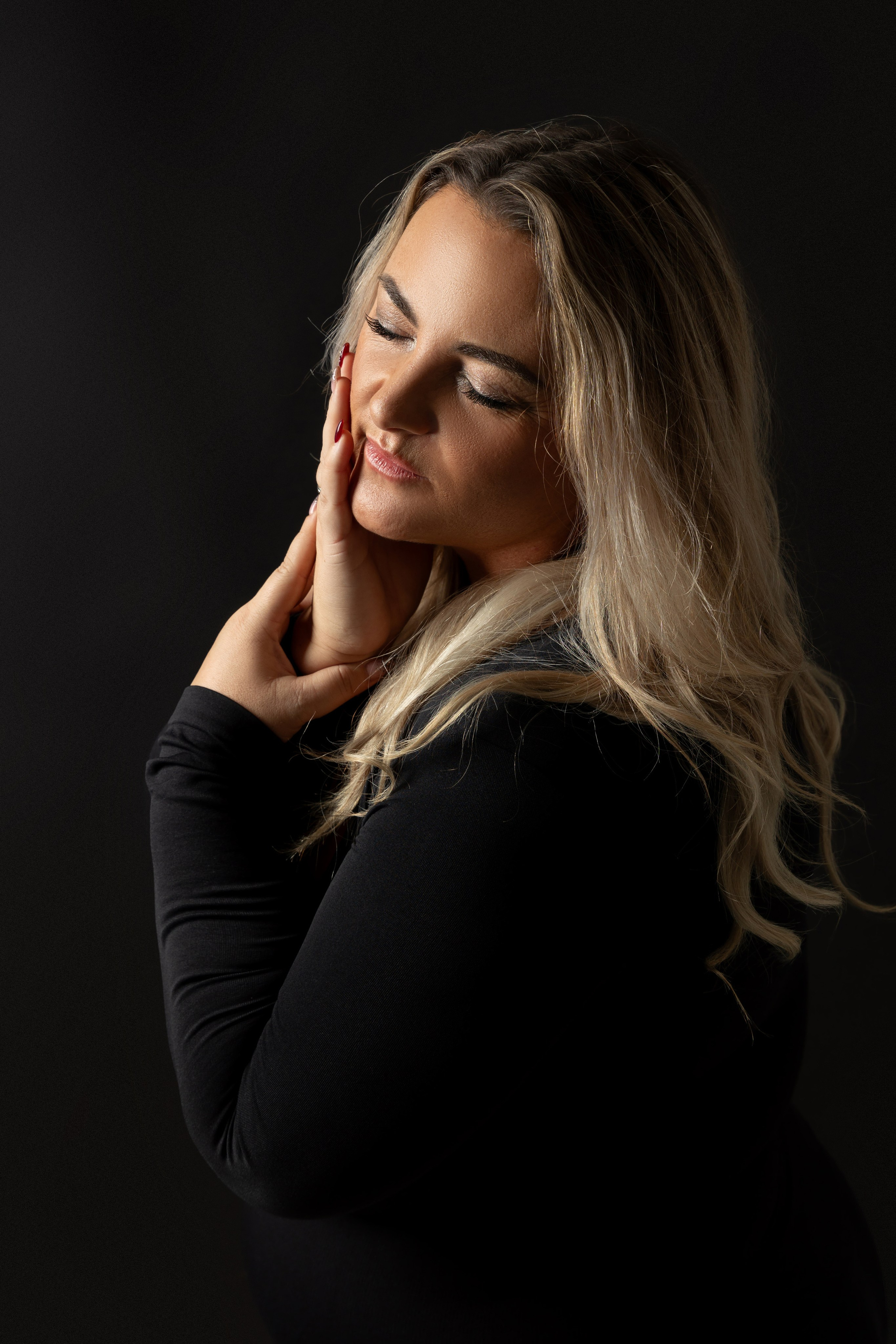 "Frau mit geschlossen Augen, die Hände sanft an das Gesicht gelegt, in verträumter Atmosphäre."