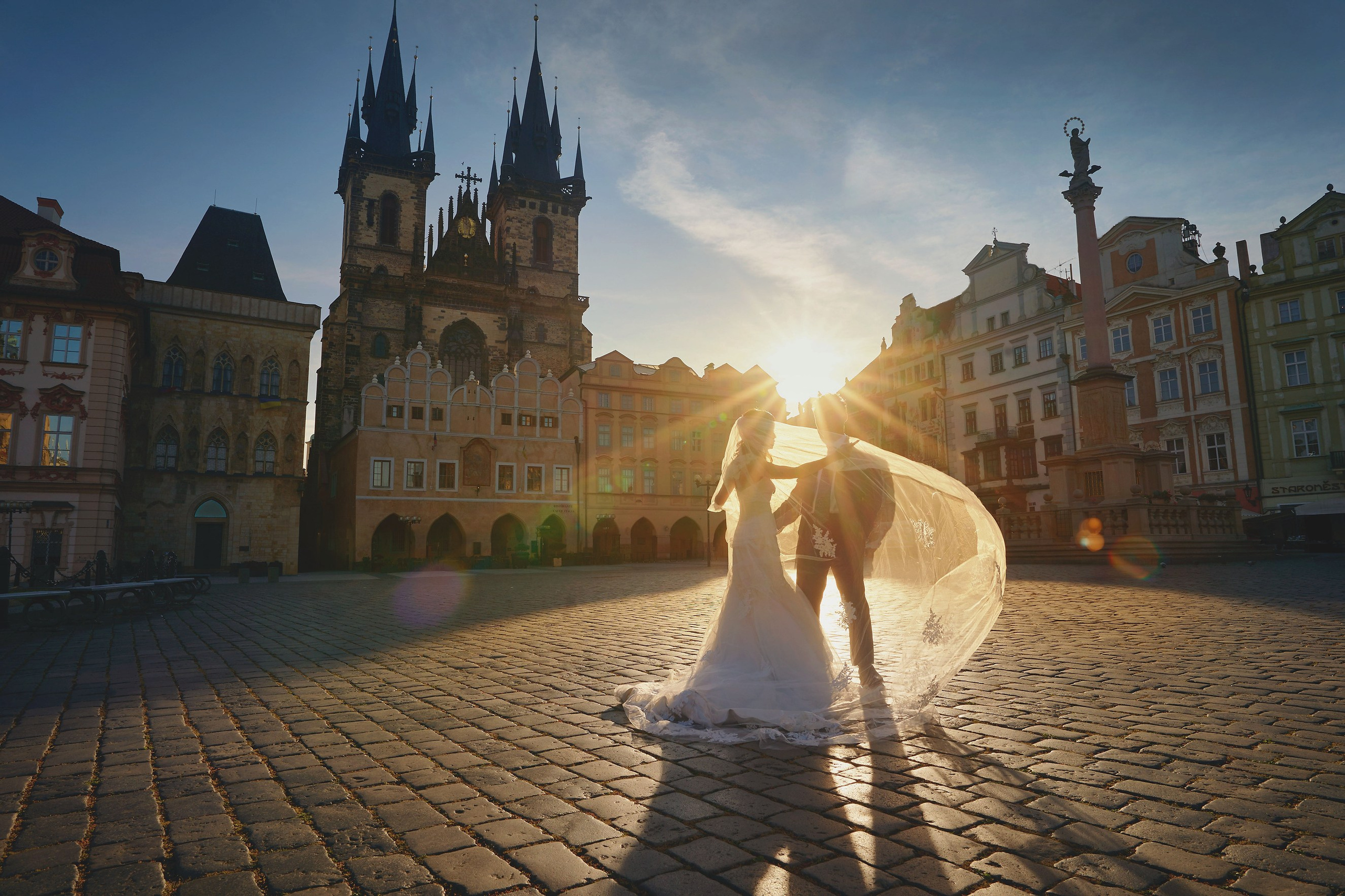Bride Eva flipping veil in silhouette with groom Conan behind in Old Town Square at dawn.