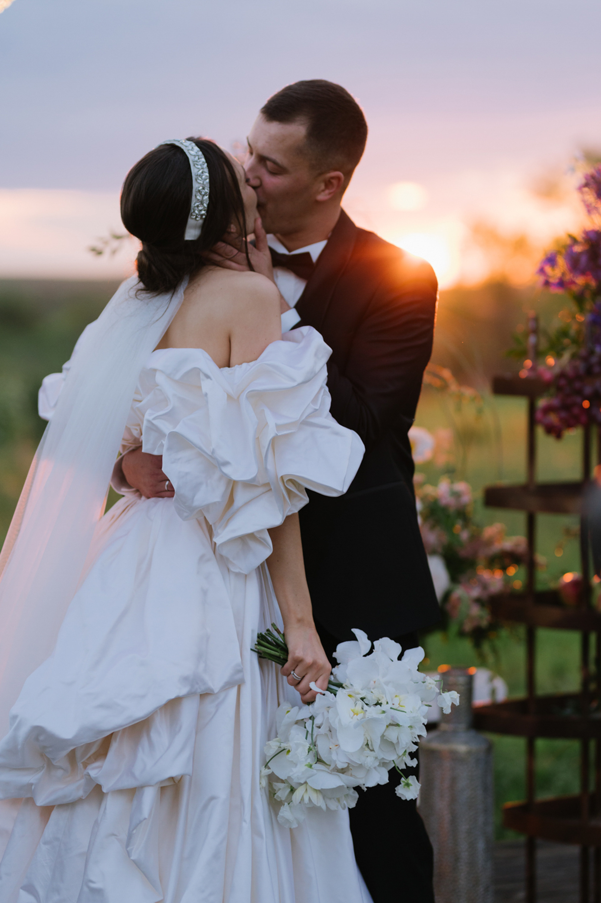 a bride and groom kissing in front of a sunset