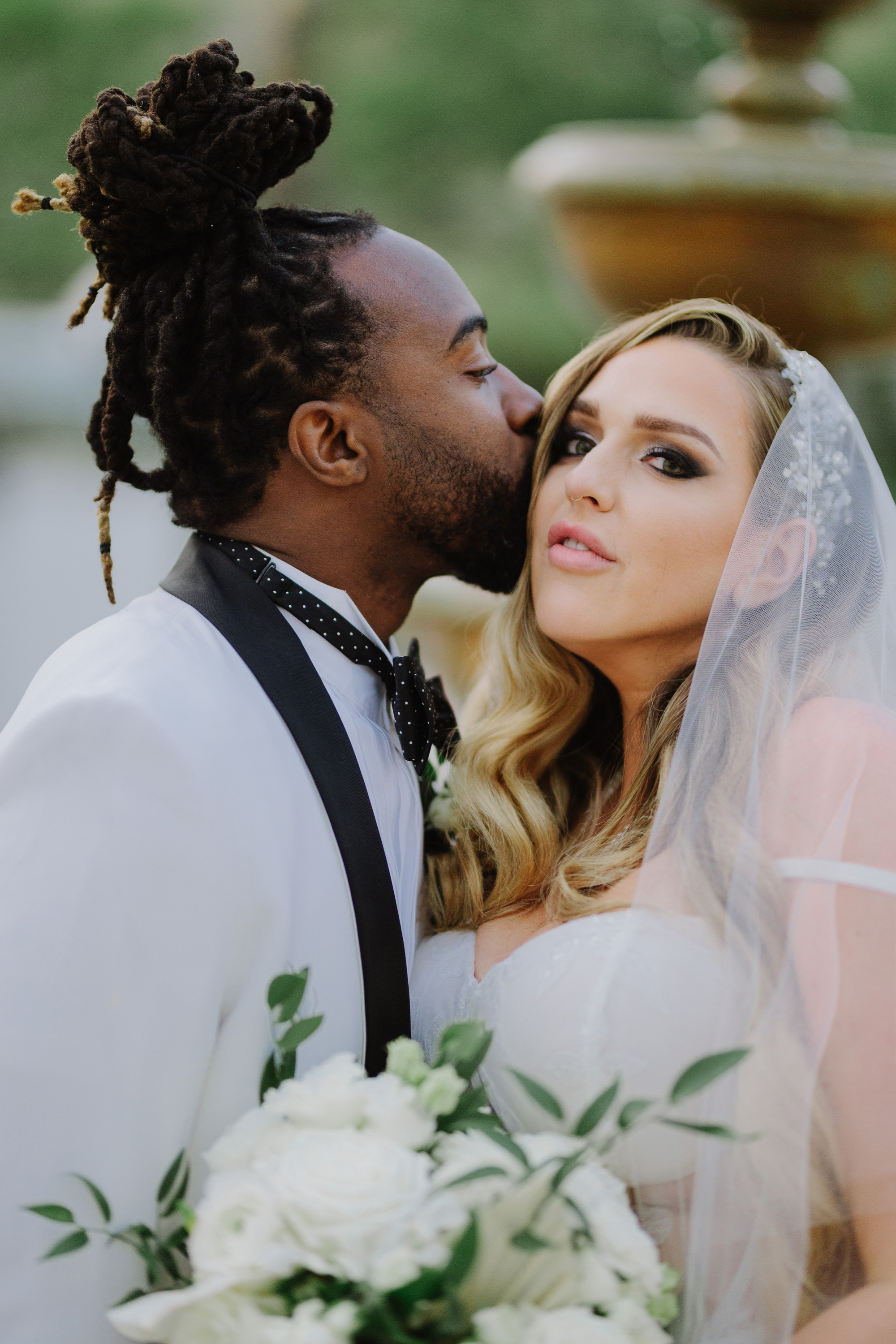 a bride and groom kissing in front of a fountain