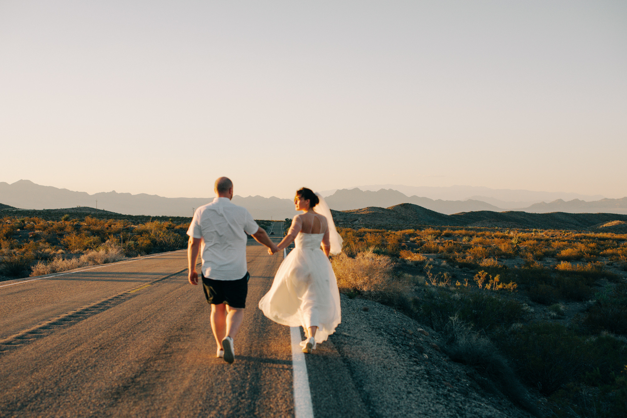 a bride and groom walking down a dirt road