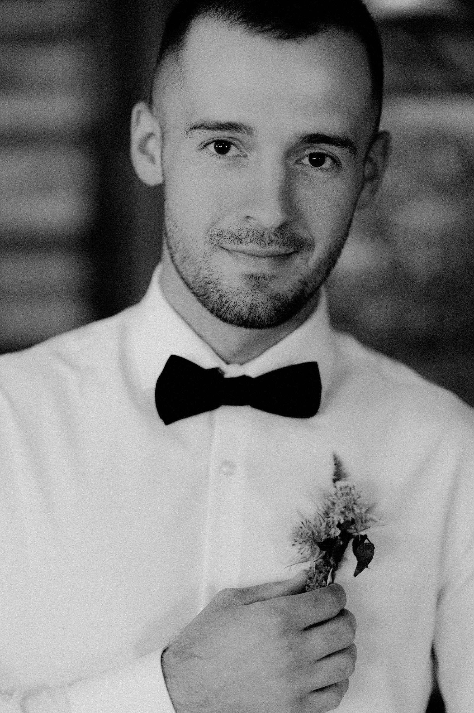 a man in a white shirt and bow tie holding a flower
