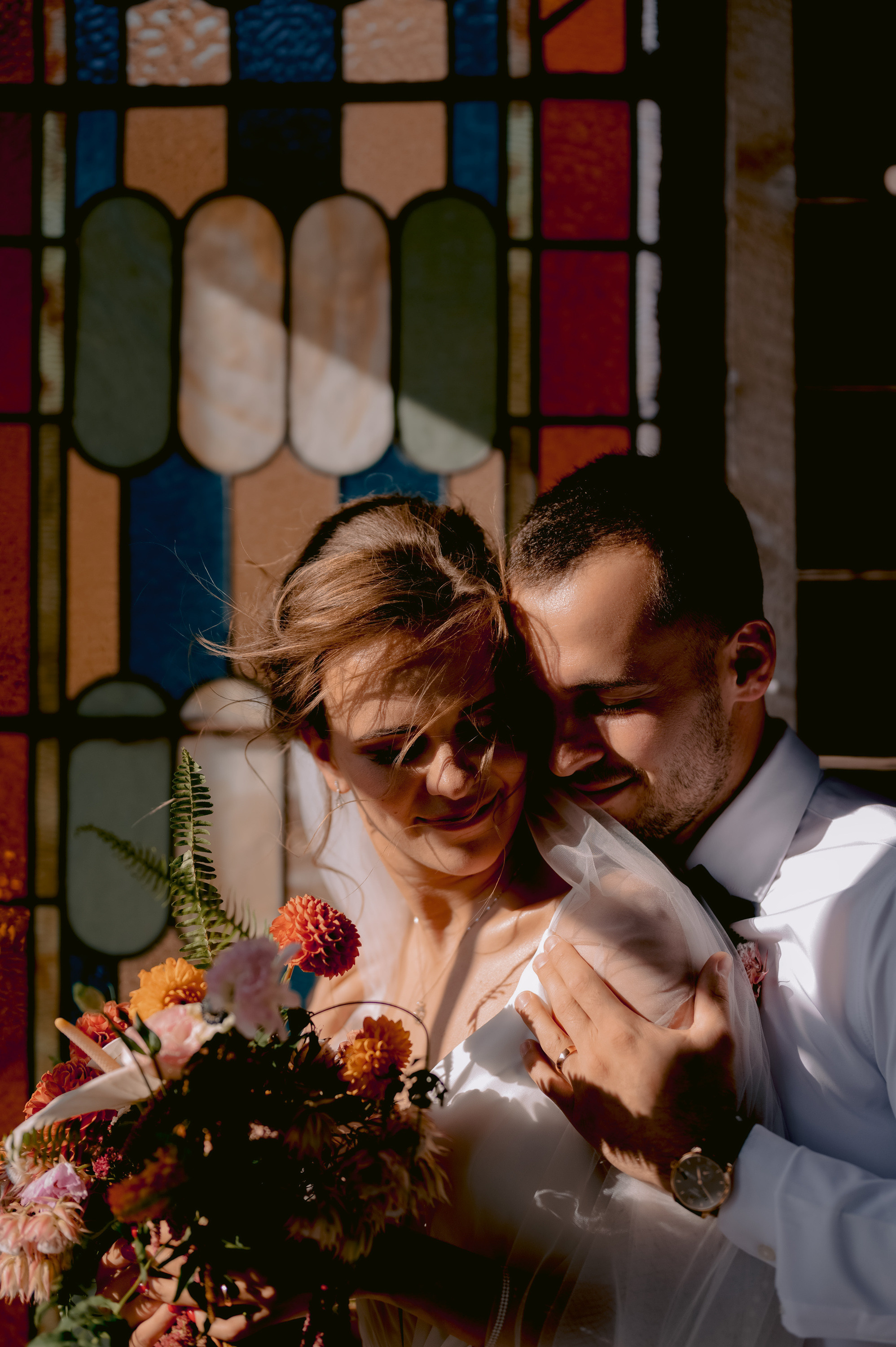 a bride and groom are standing in front of a stained stained glass window