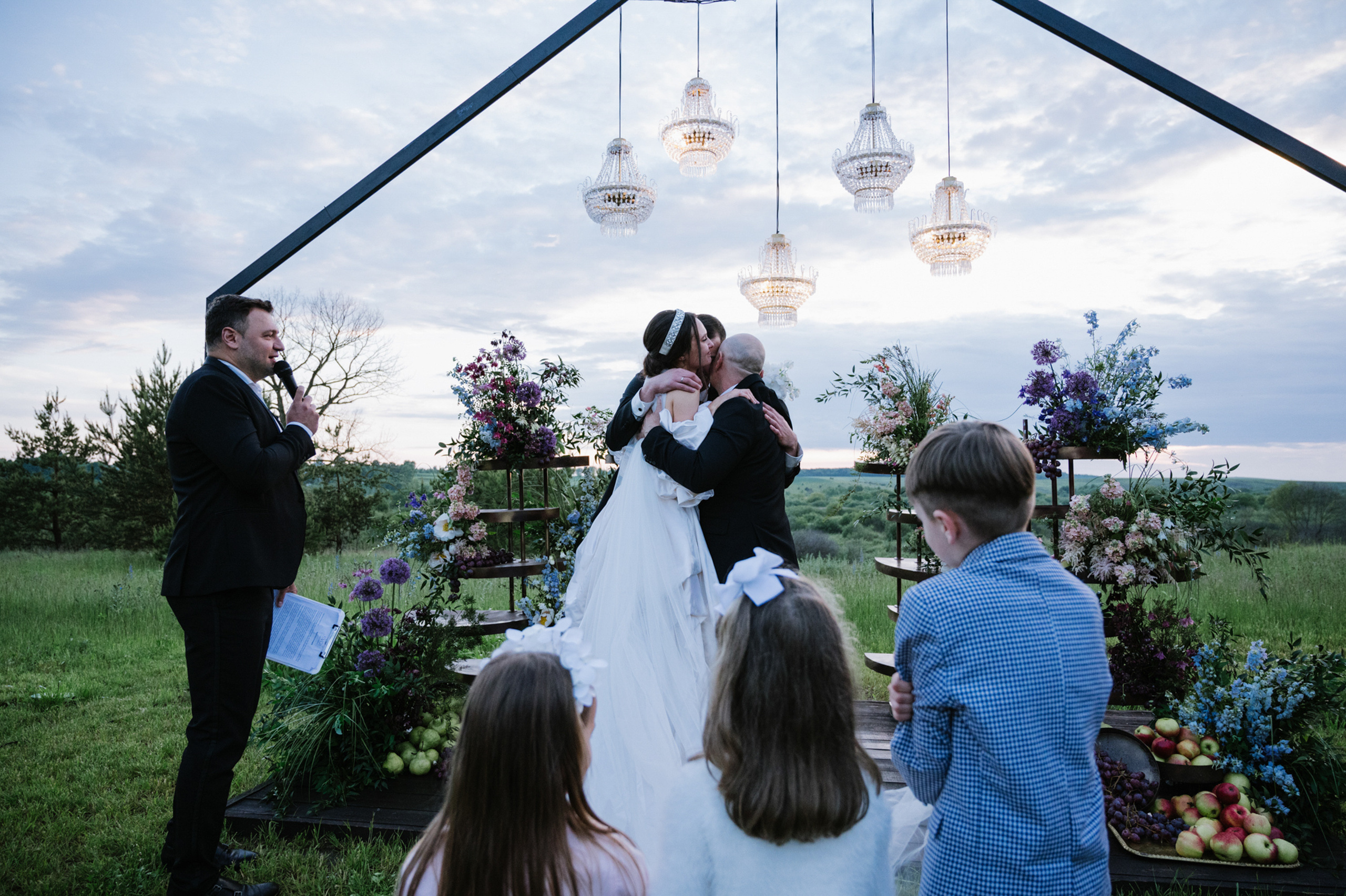 a bride and groom kiss as their children look on