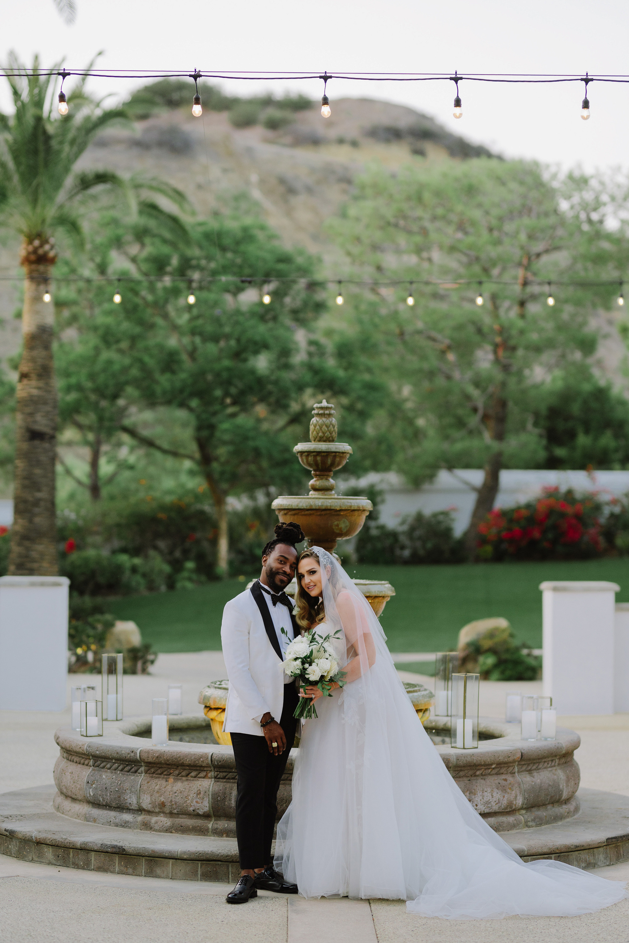 a bride and groom pose for a photo in front of a fountain