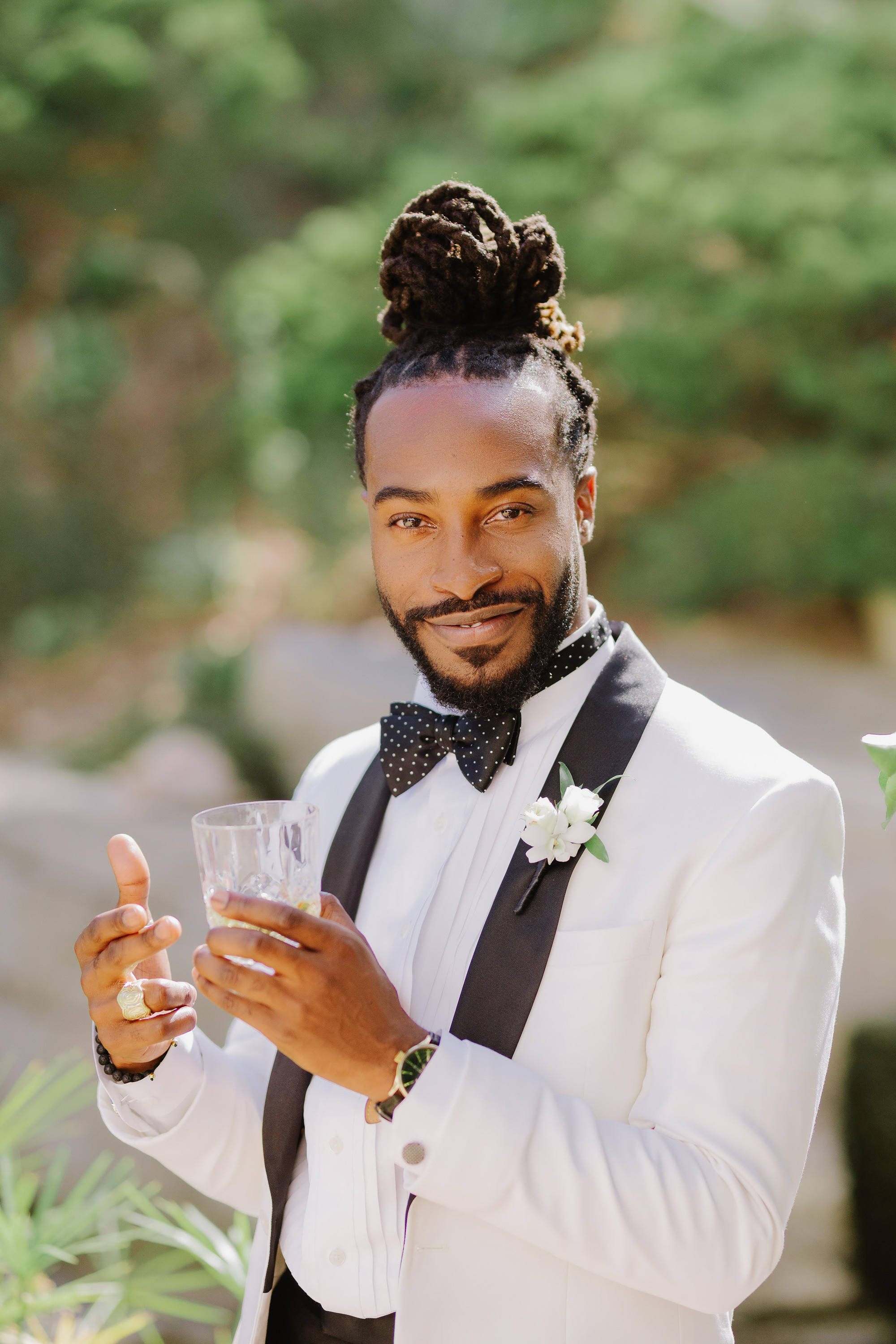 a man in a white suit and bow tie holding a glass