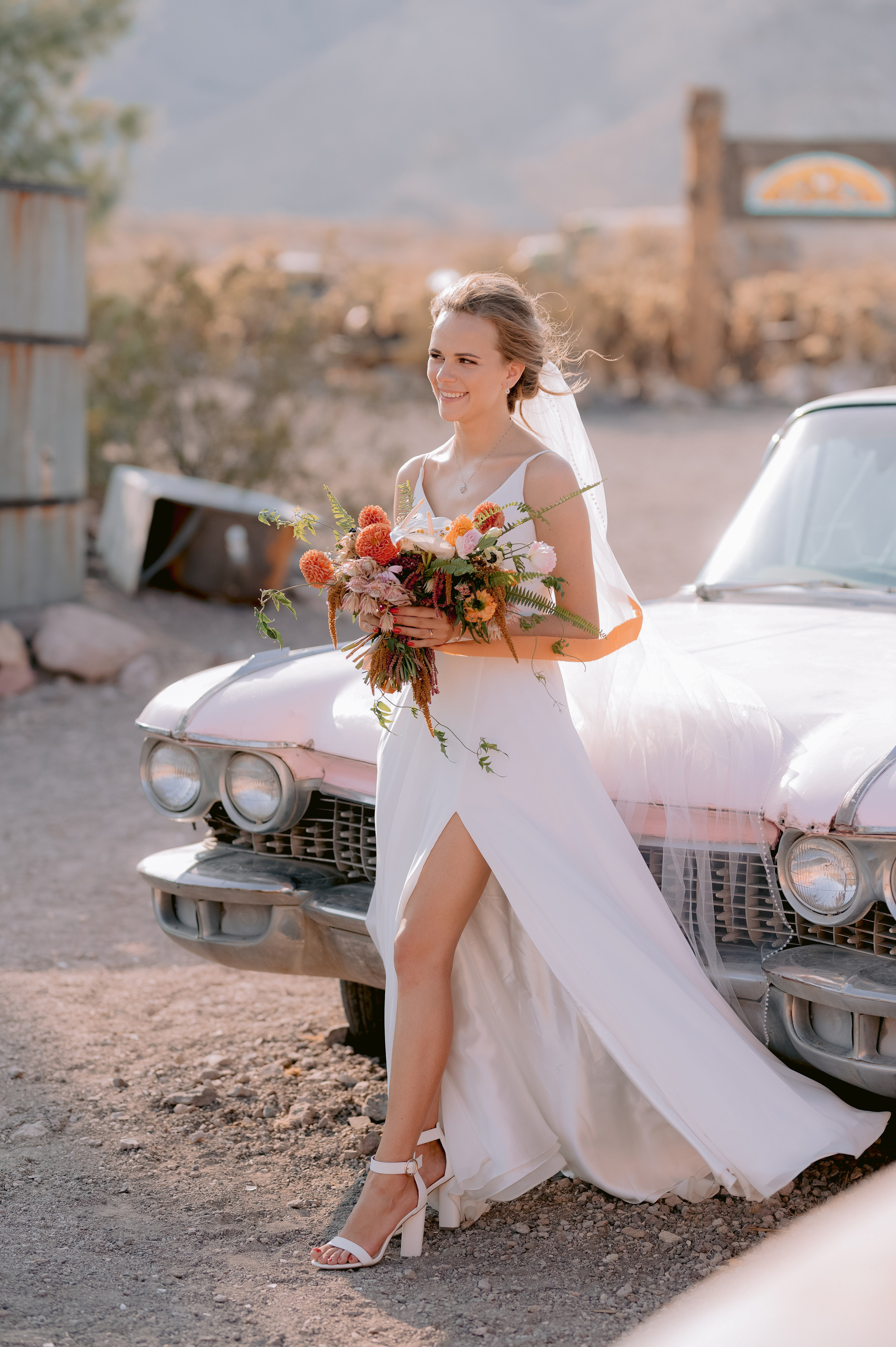 a bride sitting on the hood of a vintage car