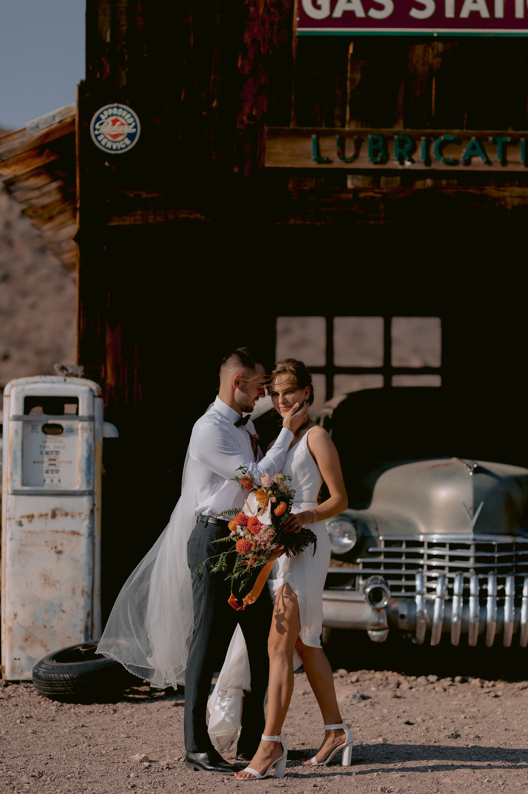 a bride and groom kissing in front of a gas station