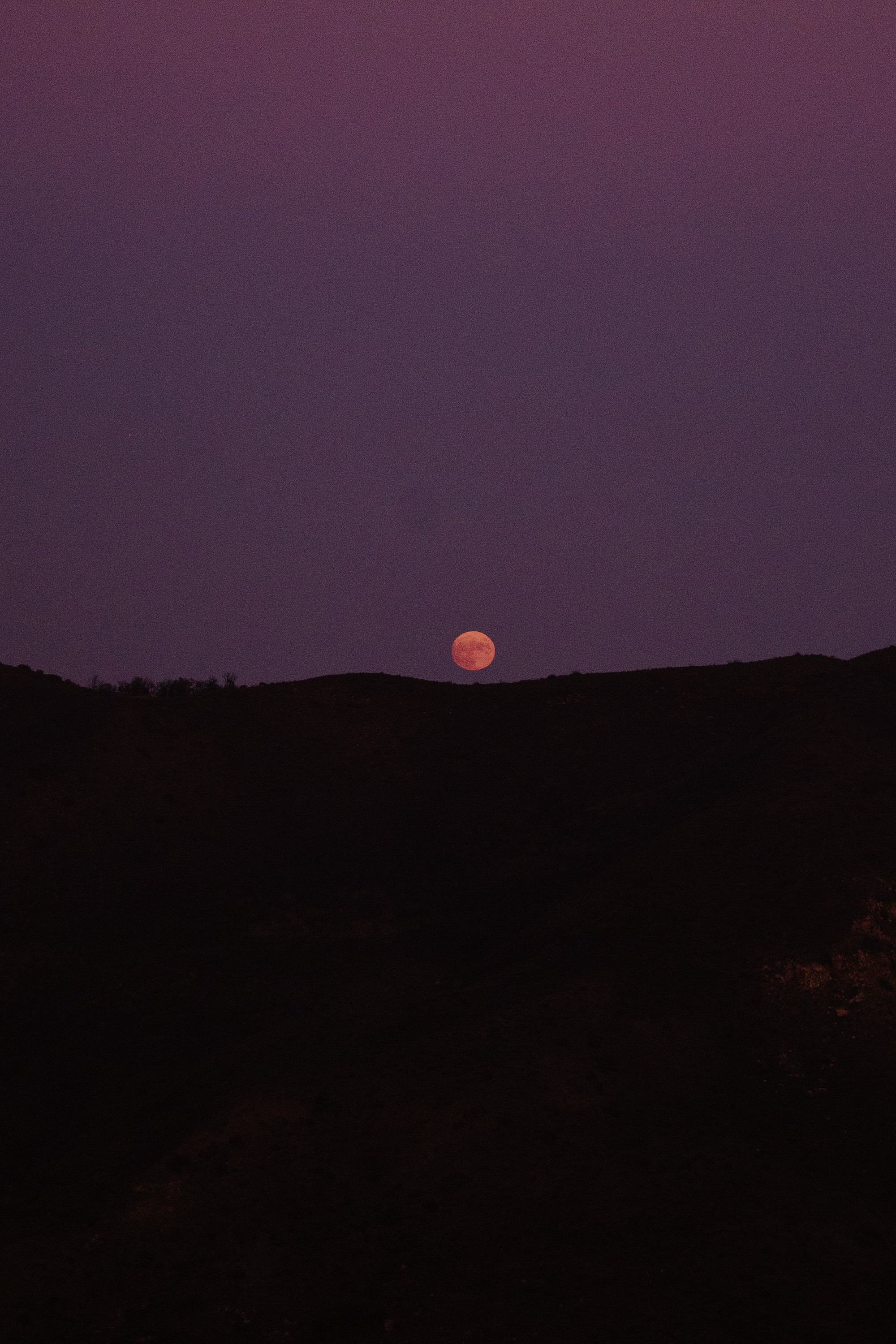 a full moon is seen in the sky above a hill
