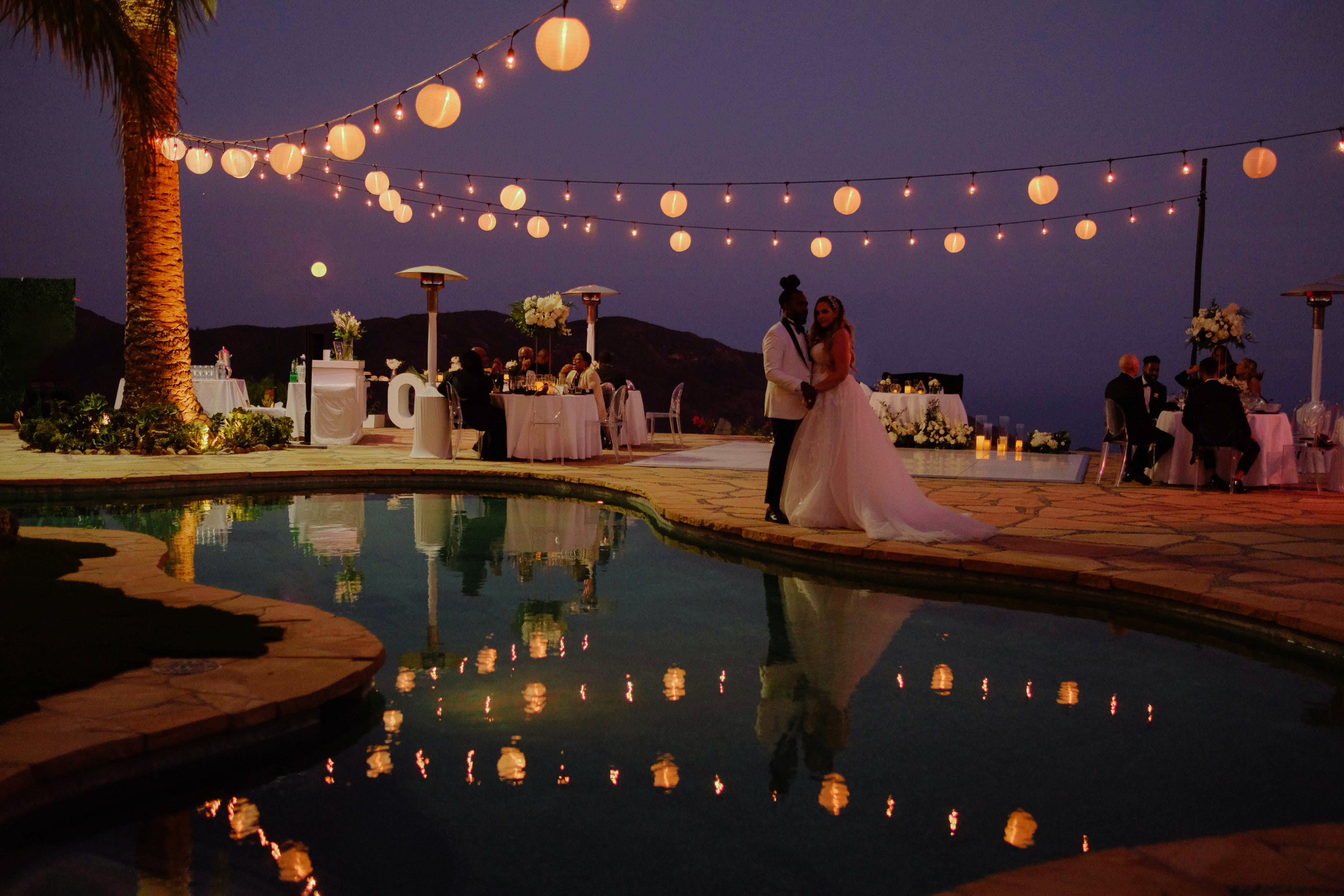 a couple standing next to a pool with paper lanterns