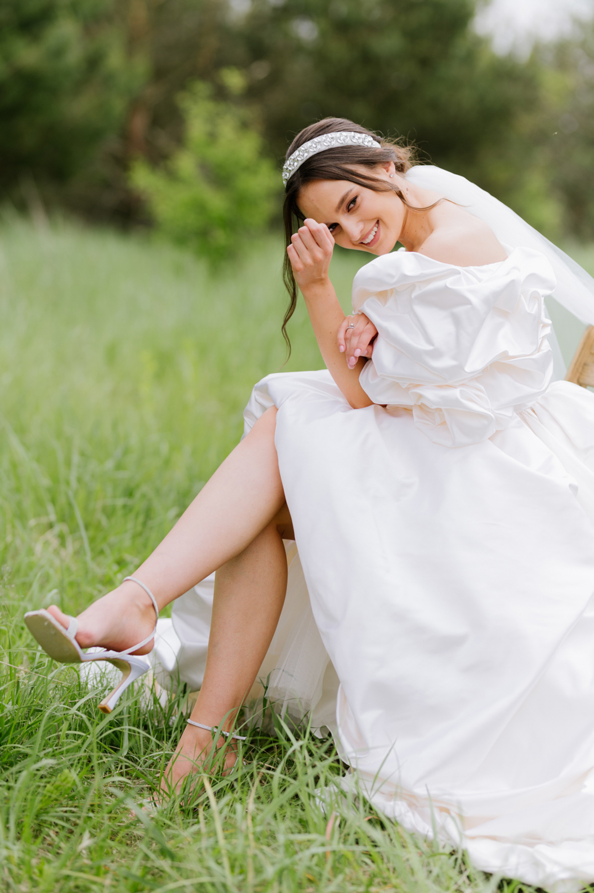 a bride sitting in the grass with her shoes on