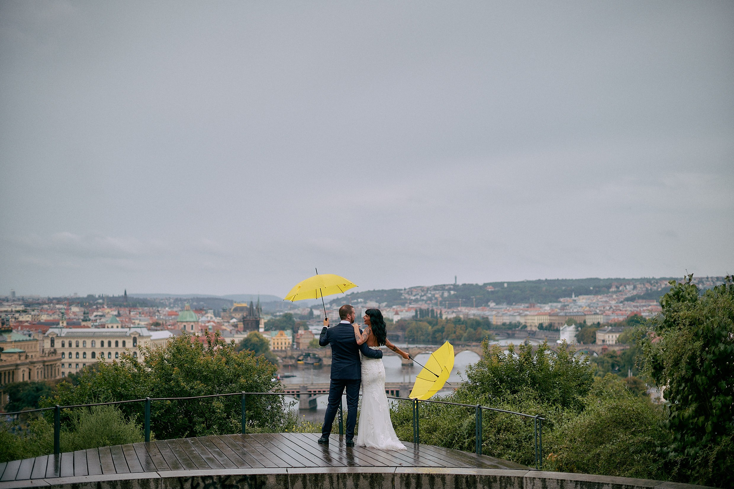 Newlyweds hugging in rain at scenic Letná Park viewpoint Prague.