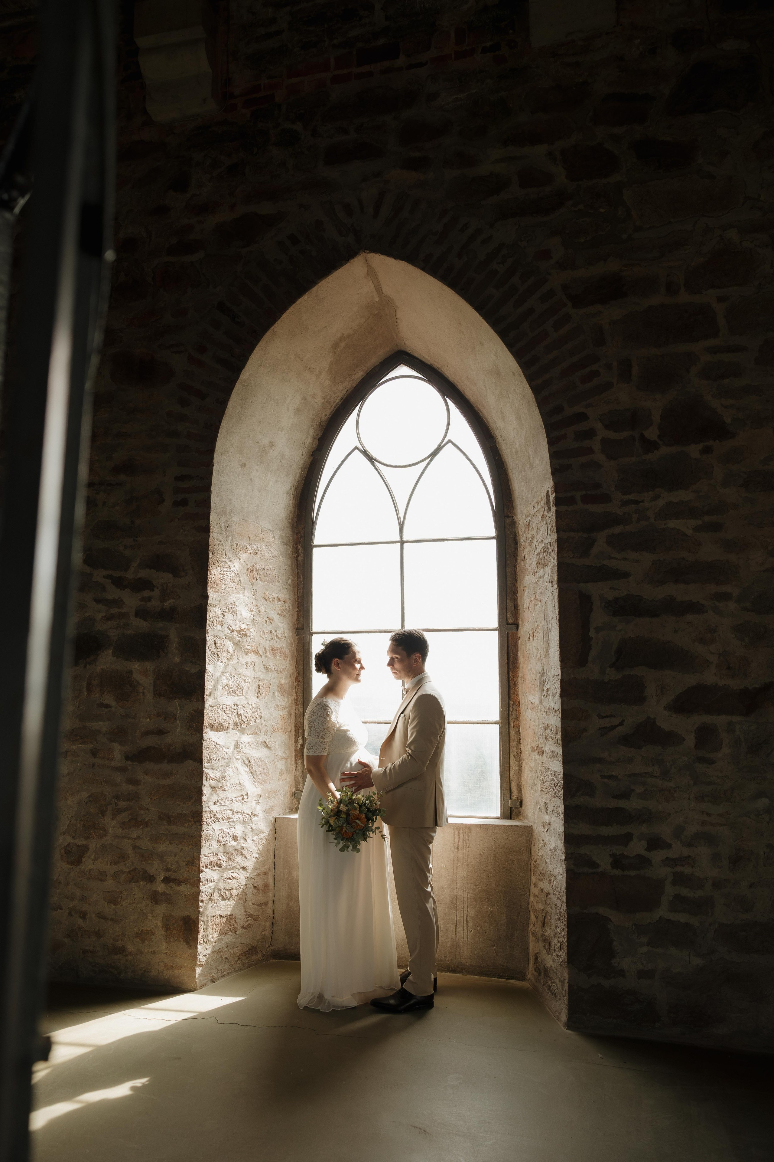 Brautpaar im Gegenlicht vor einem historischen Bogenfenster im Inneren der Diedrichsburg, Heiraten auf der Diedrichsburg