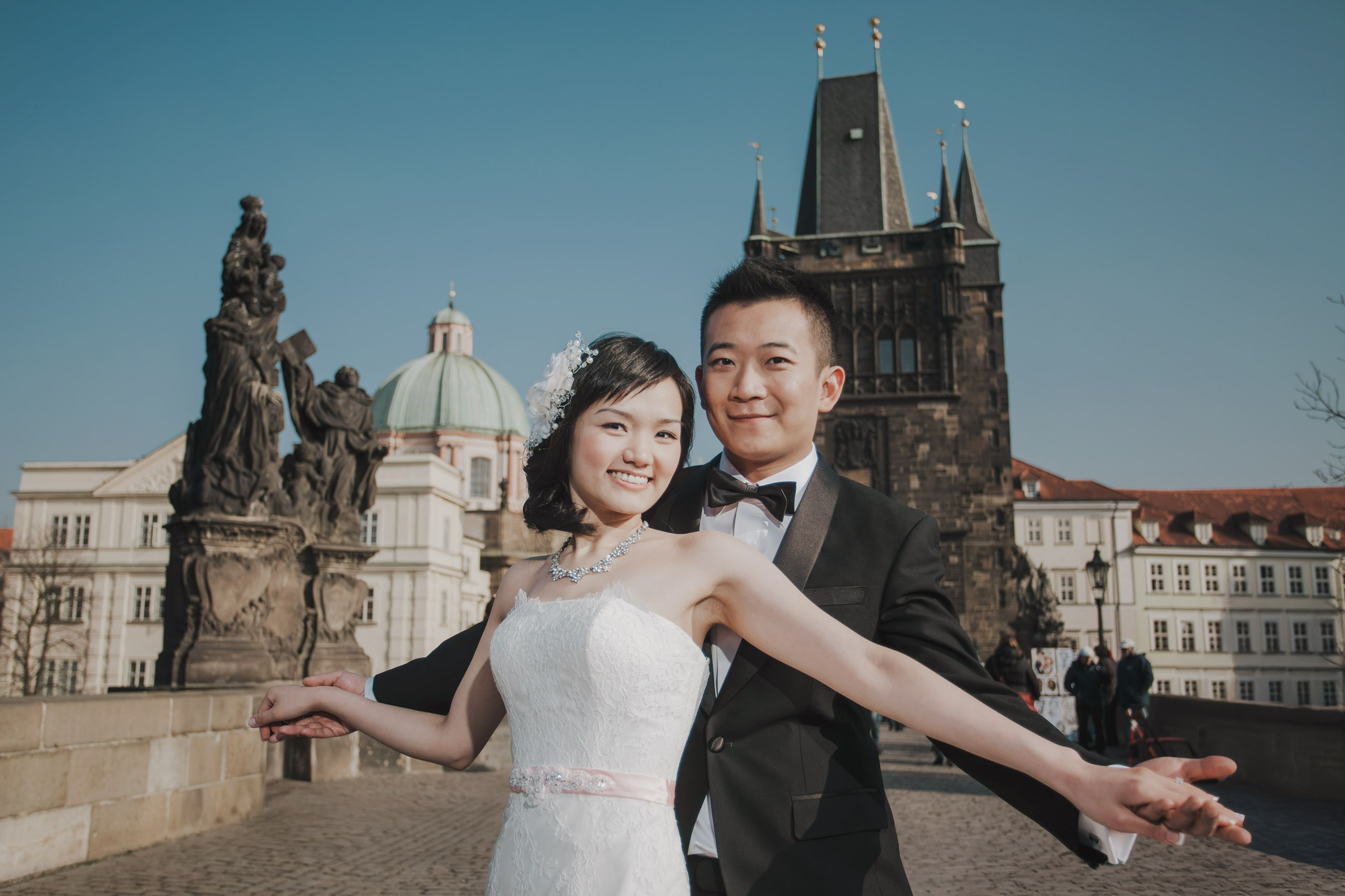 The wedding attired Hong Kong bride & groom pose for a photo atop the world famous Charles Bridge in Prague.