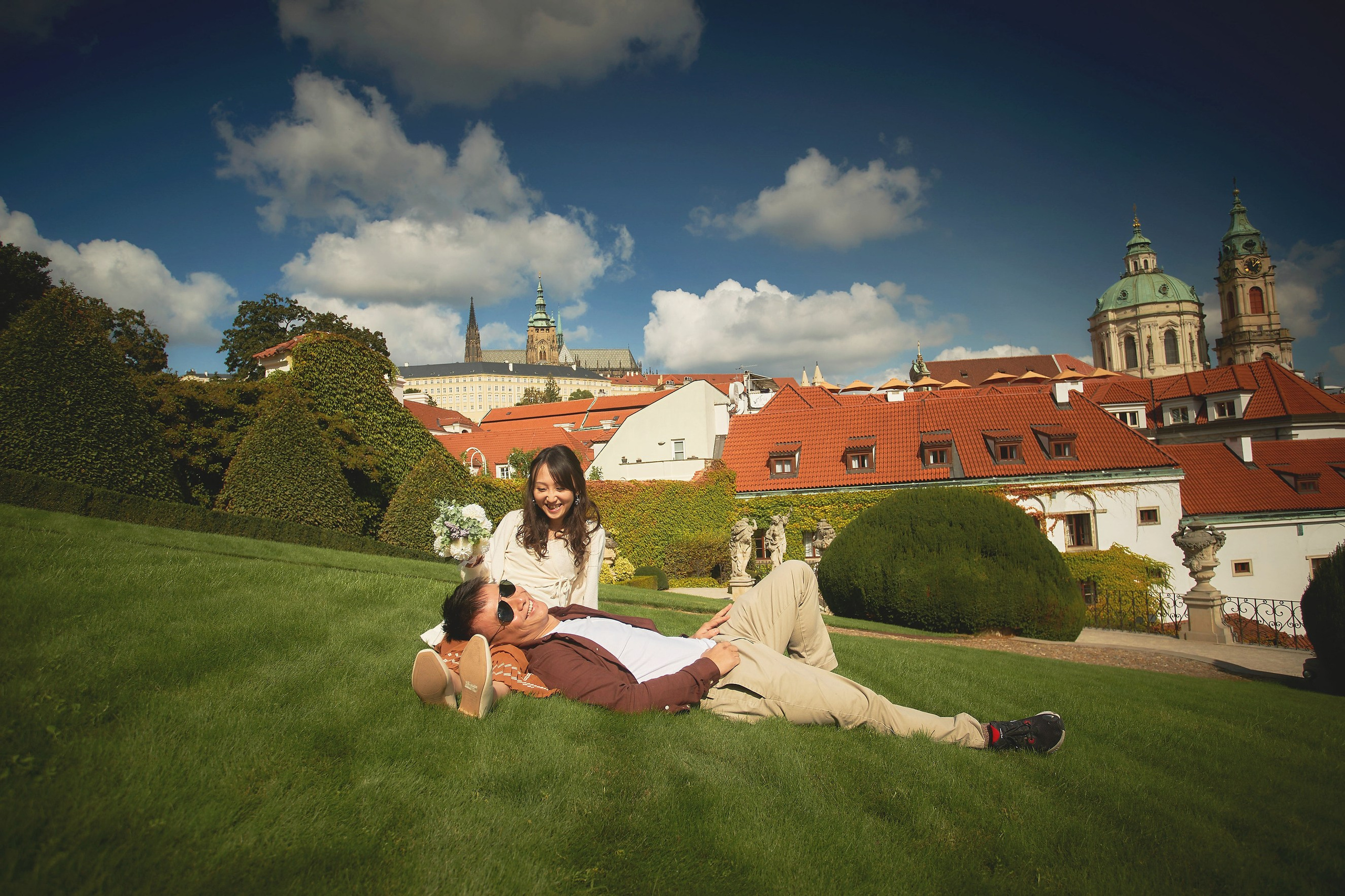 Groom Conan lying in bride Eva’s lap, smiling on Vrtba Garden lawn, Prague.