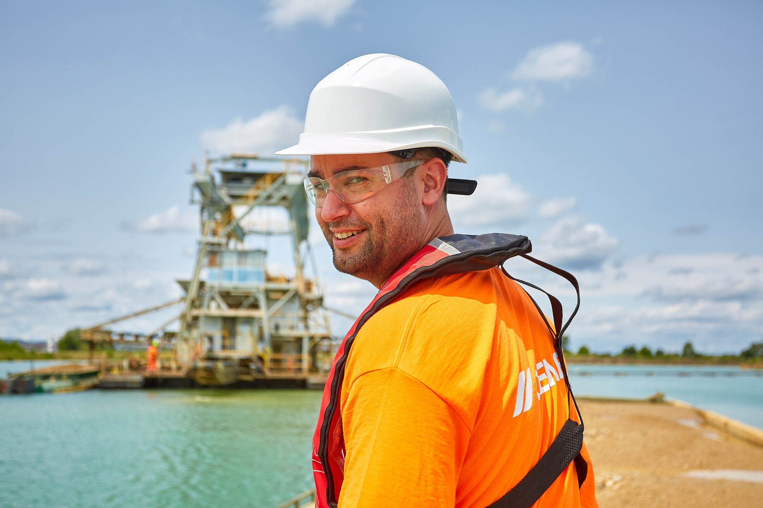 A confident, smiling man looks towards the camera as a barge makes its way to a floating industrial site in Prachovice, Czech Republic.