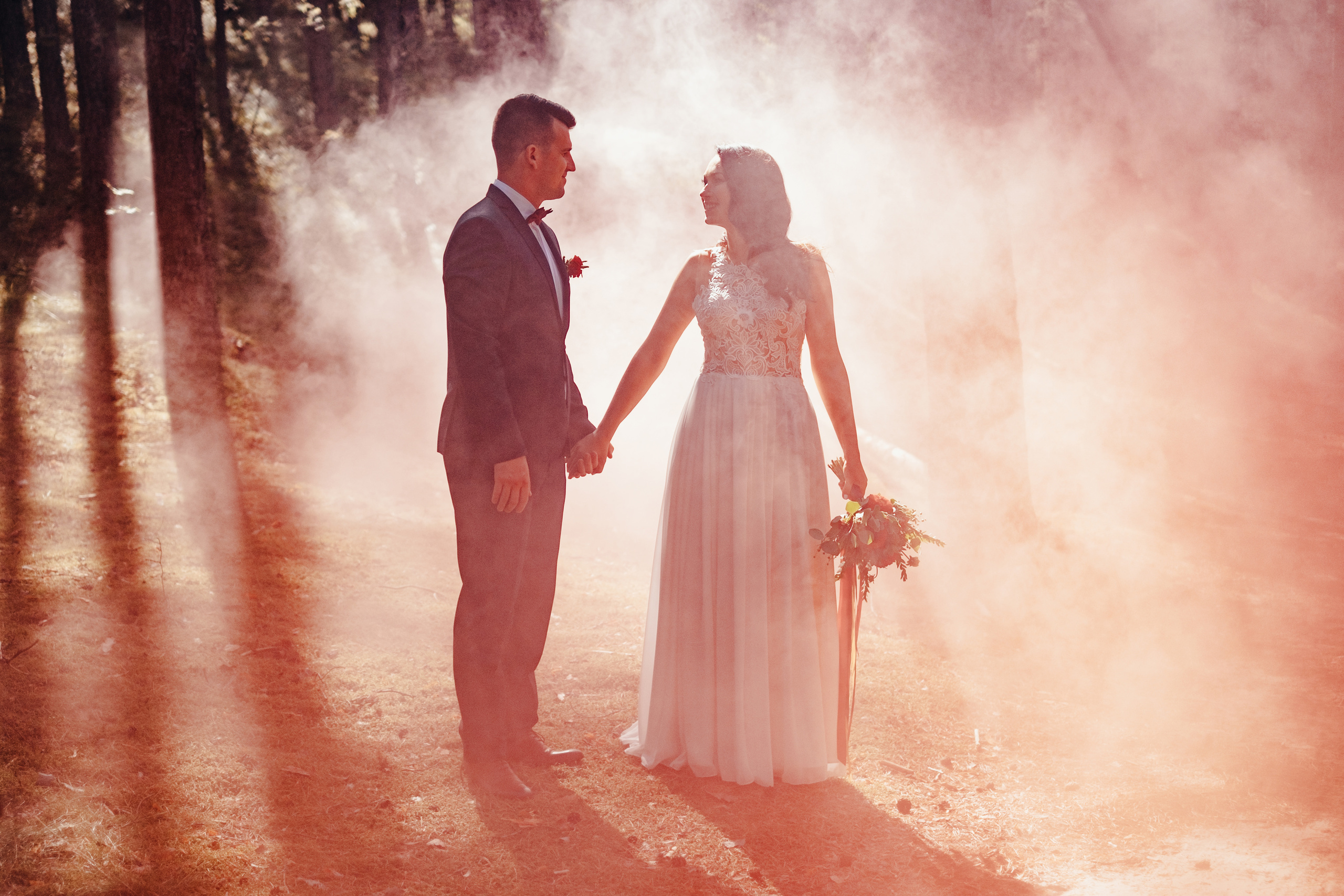 Dūmu sveces kāzu fotosesija. Fotosesija mežā. Līgava un līgavainis sadevušies rokās, dūmu sveces dūmos ieskauti.