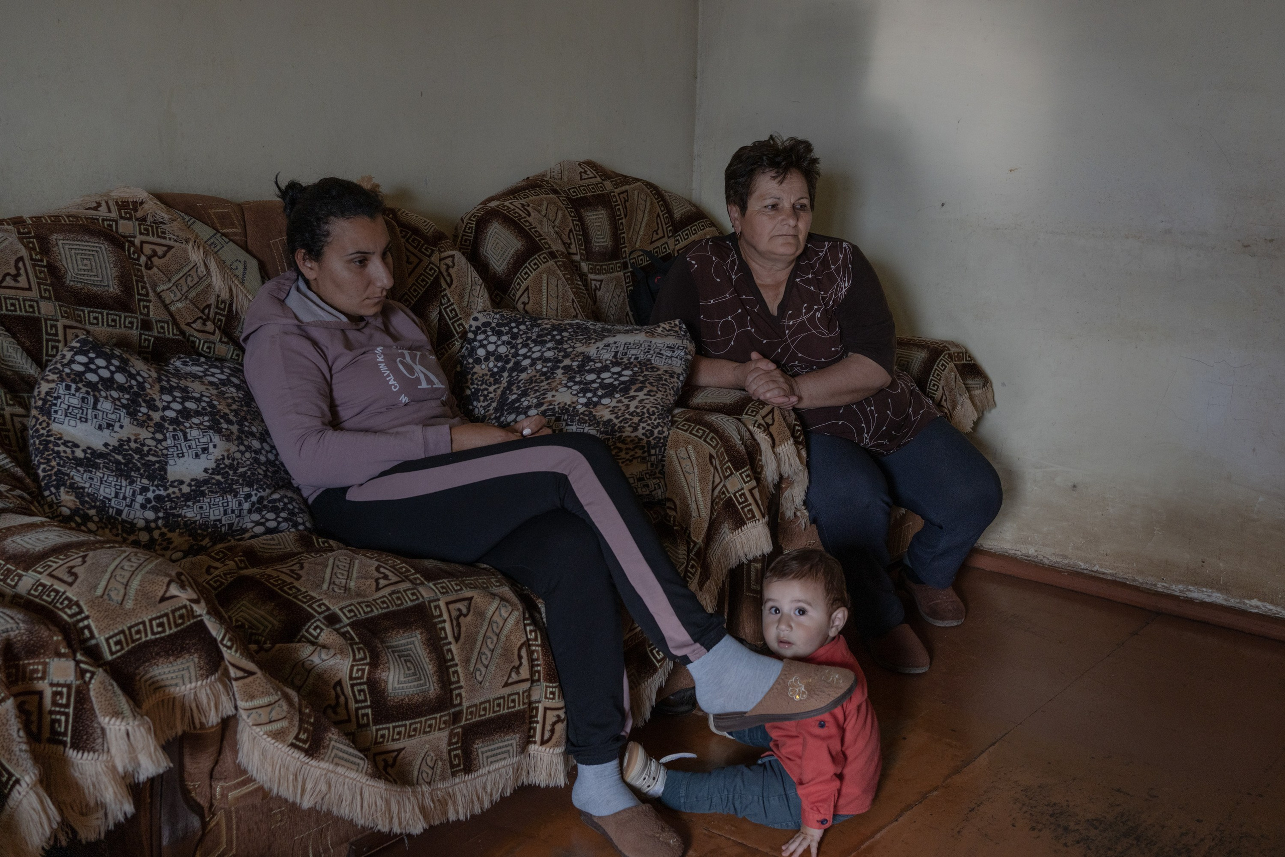 Anahit (right) lost her son during the 2020 Nagorno-Karabakh war. She is sitting in the living room where her son's portrait is hanging. Anahit and her husband are often visited by their family. Syuzi (left) is paying a visit with her children. Anahit and Syuzi were talking about daily life when a moment of silence broke their conversation.