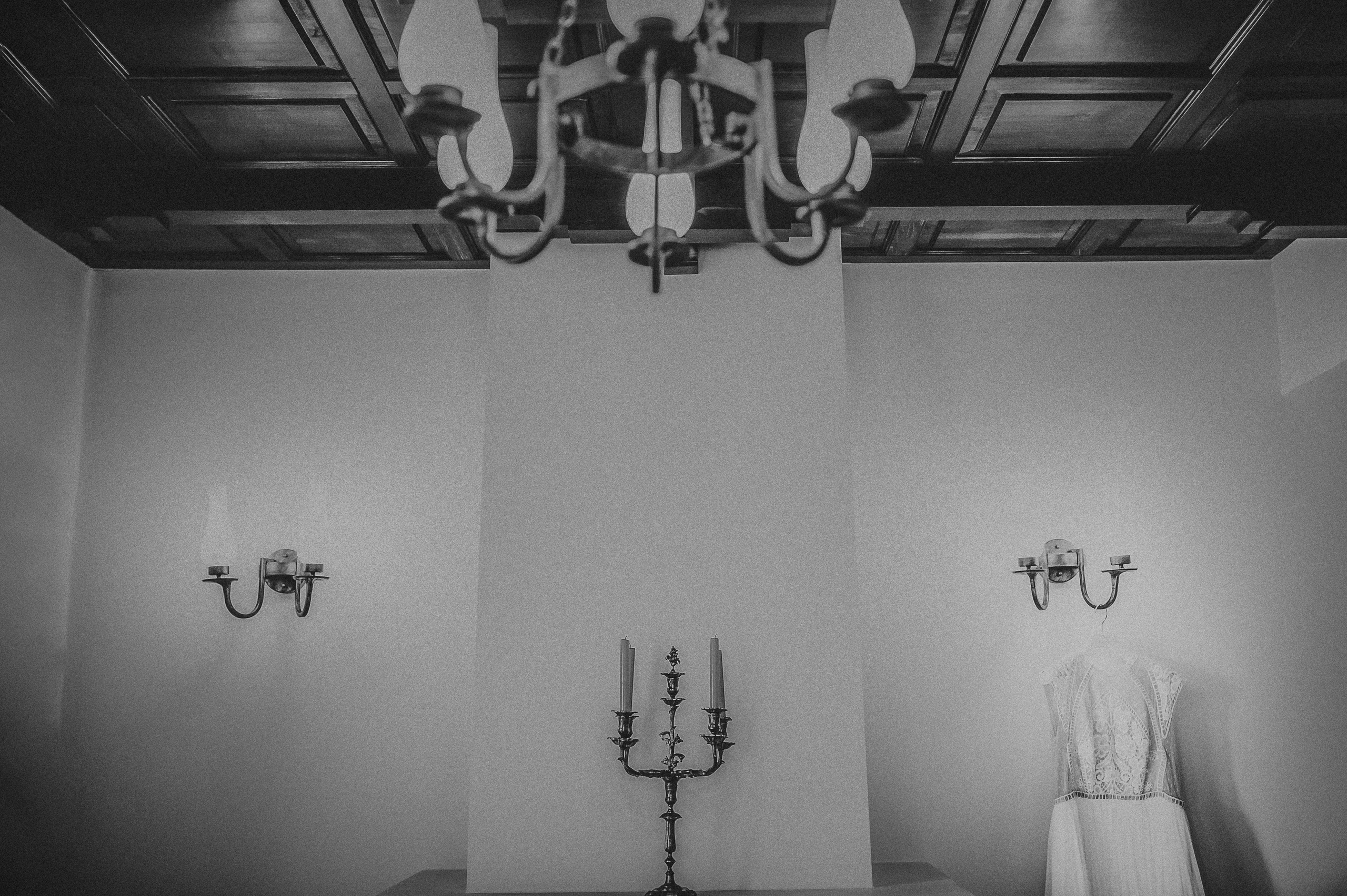 Detaliu alb-negru cu rochia de mireasa asezata pe un umeras care atarna de o lunstra.