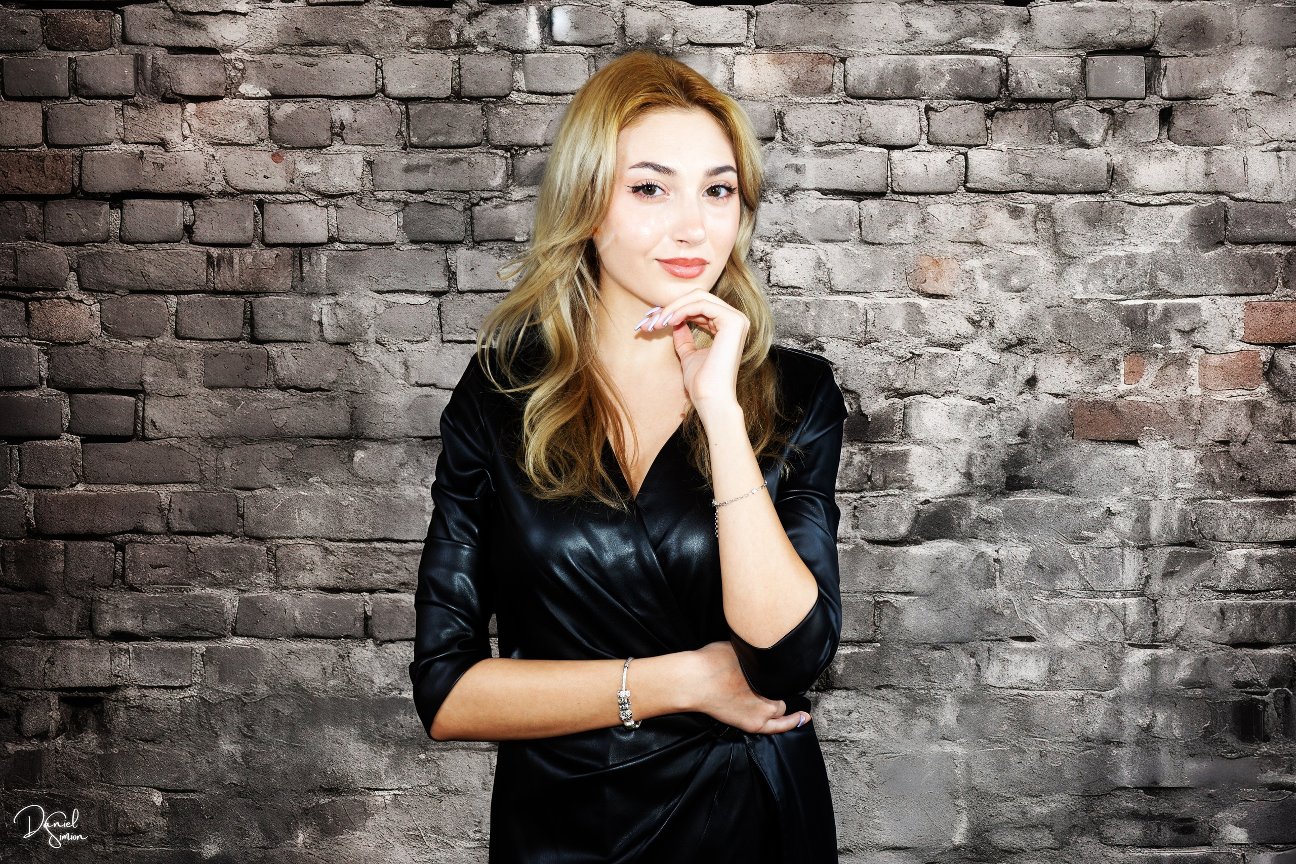 Young woman posing in black dress in front of a brick wall.