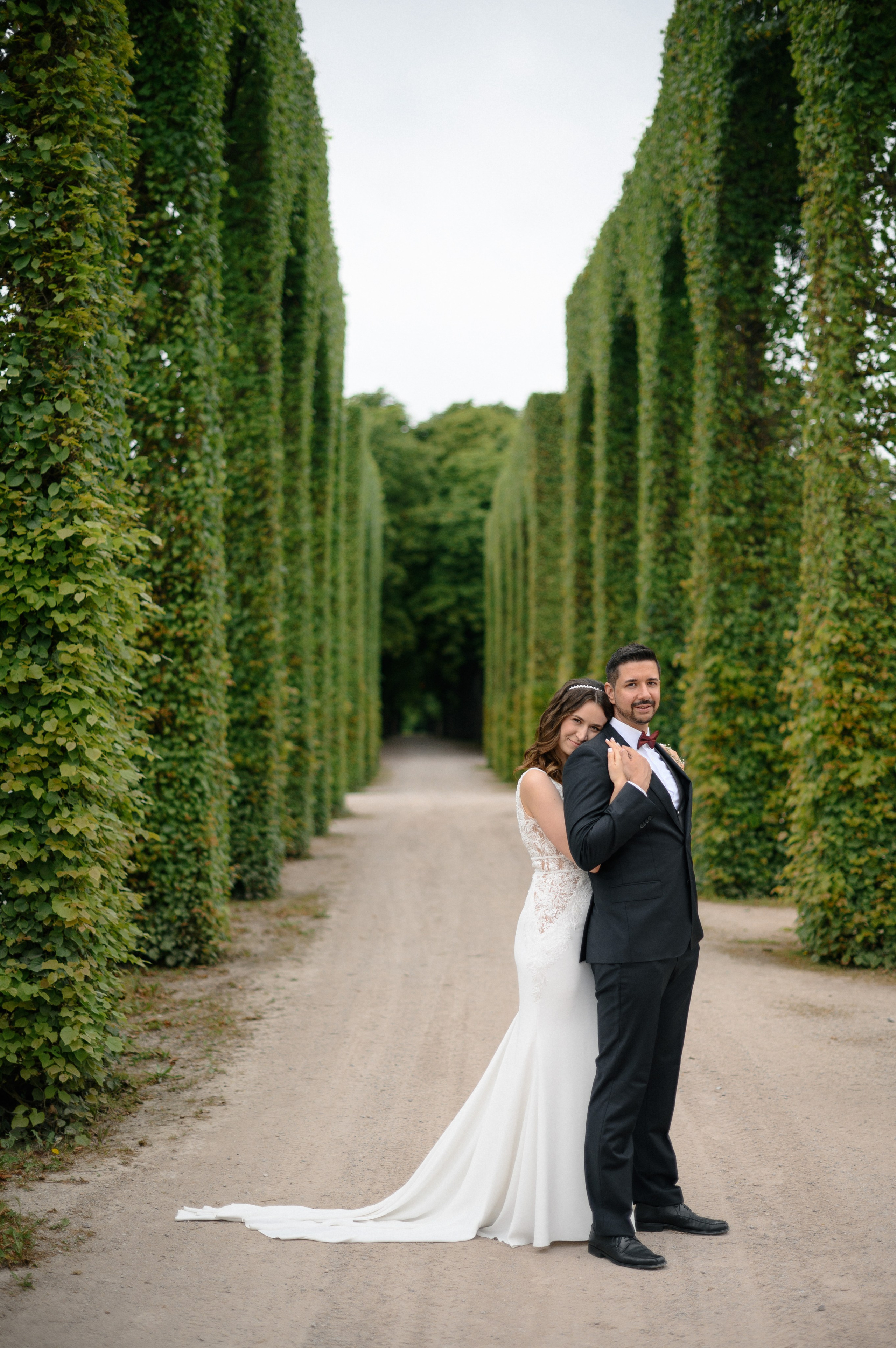 Brautpaar zwischen symmetrischen Baumalleen im Schlossgarten bei der Hochzeitsfotografie